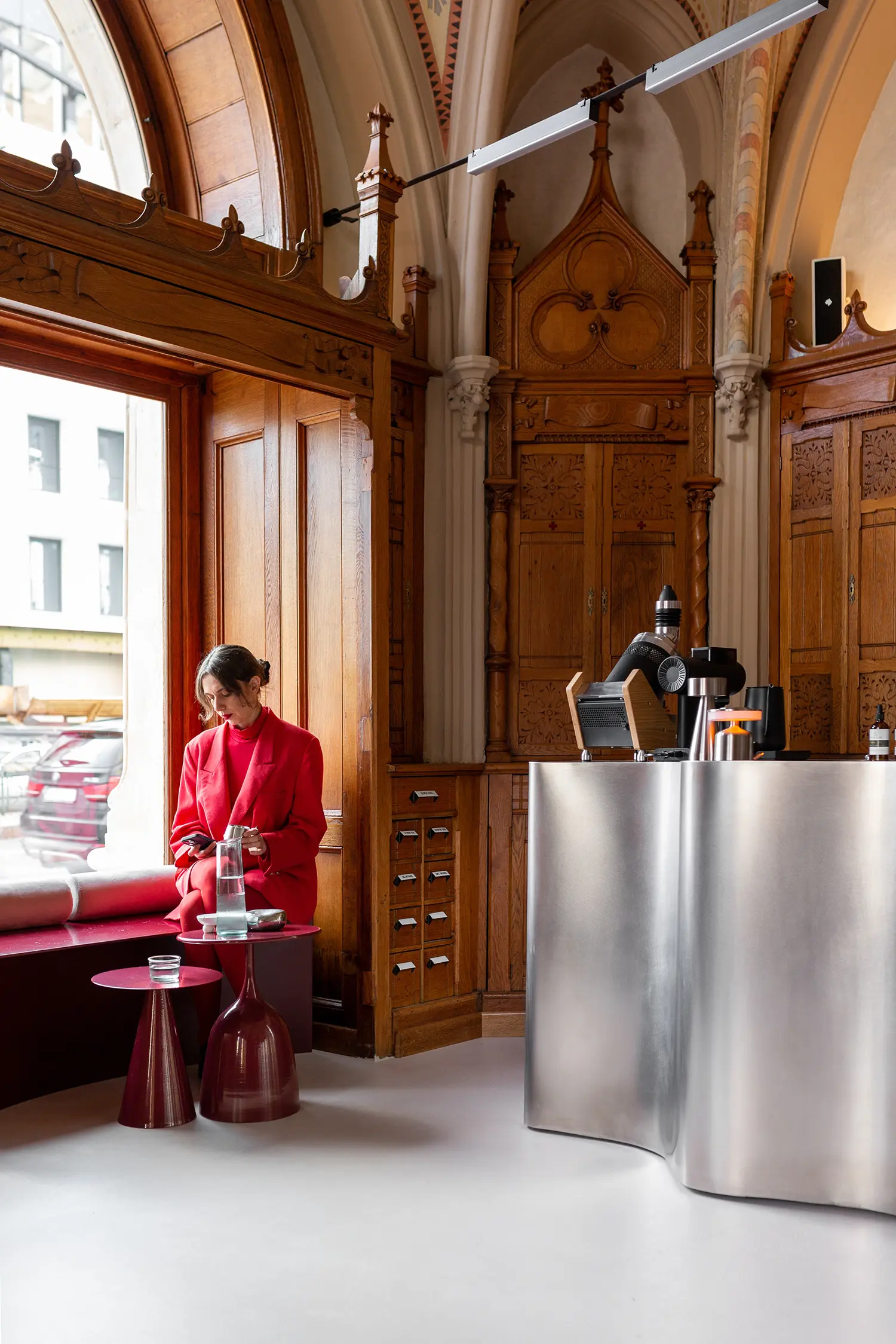 A person in a vibrant red coat sits on a deep red window bench at Laboratorium coffee shop.
