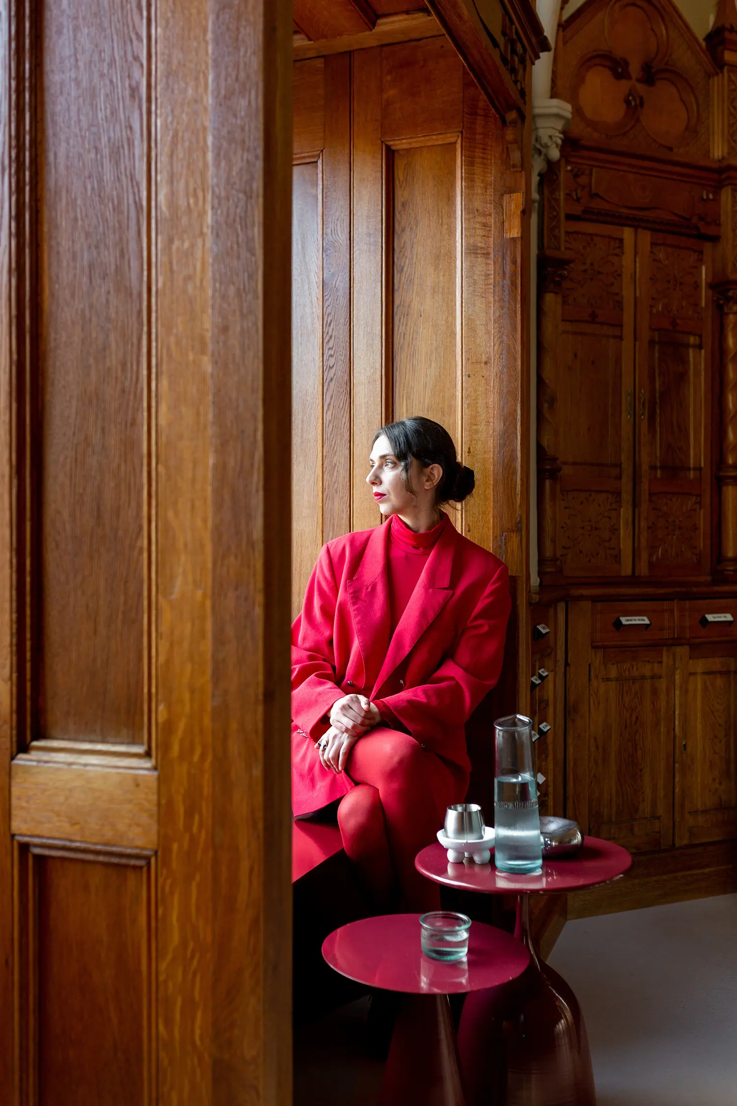 Portrait of a woman in red profile-view sitting by a large wooden window frame in Cluj-Napoca.