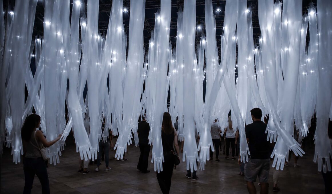 Caressing Zone by luzinterruptus, hundreds of translucent fabric arms suspended from truss structure, visitors walking beneath