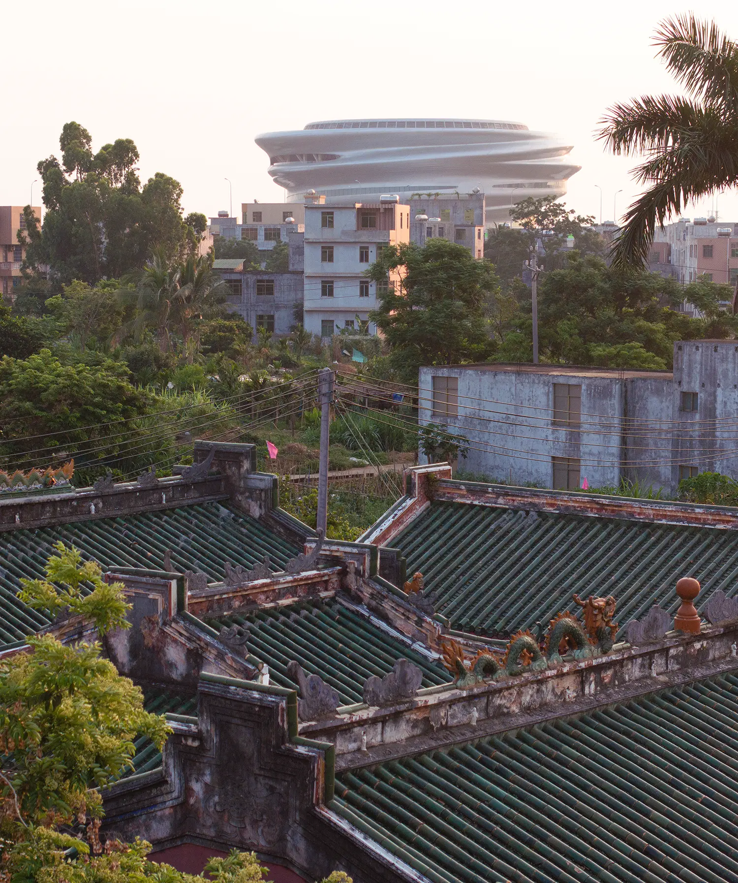 High-angle view of the Hainan Science Museum rising behind traditional green-tiled roofs in Haikou.