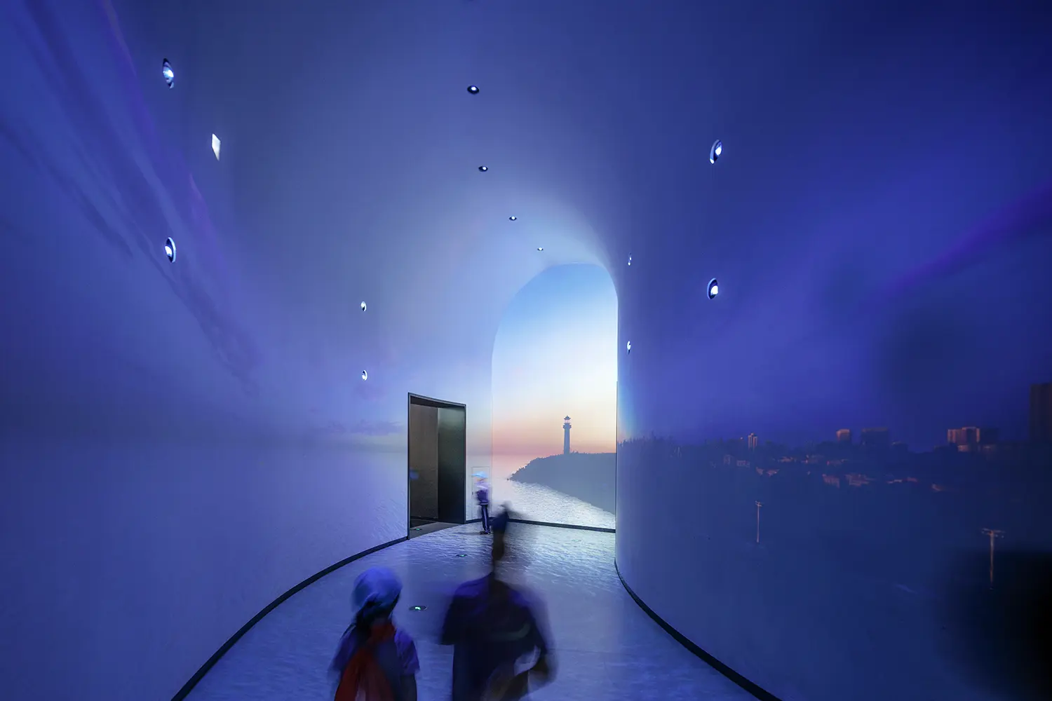 Interior of a blue-lit tunnel walkway with digital projections of a lighthouse and coastline.