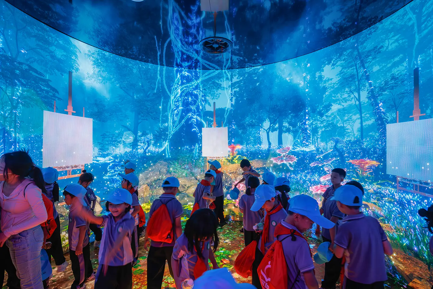 Group of school children in blue hats exploring a 360-degree digital rainforest exhibition.