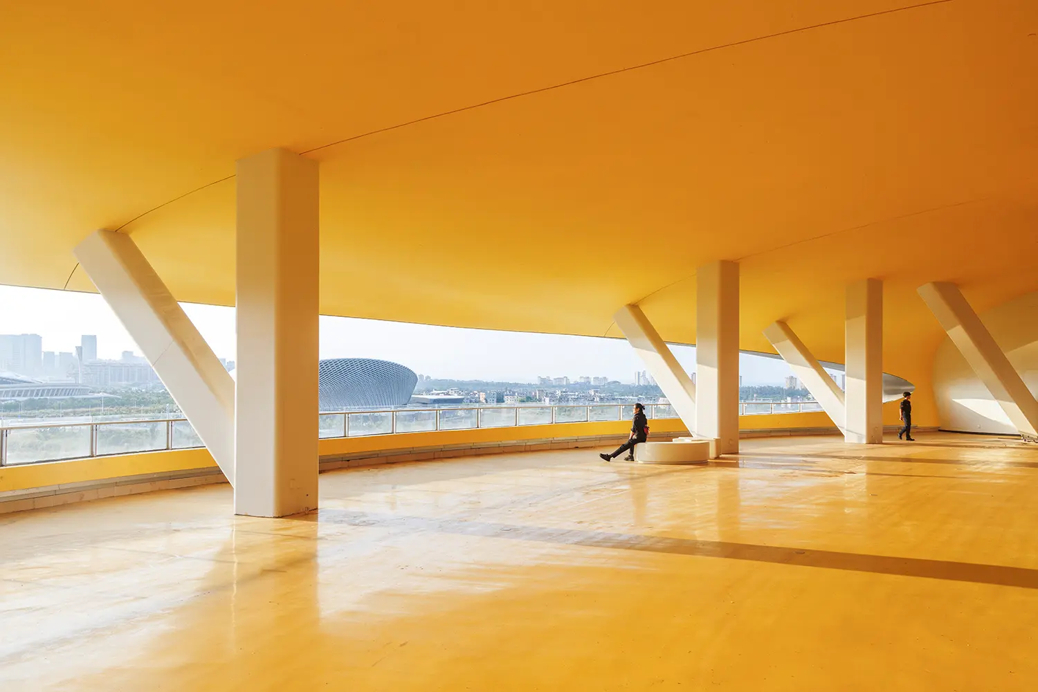 Wide view of a bright yellow shaded plaza with white structural columns looking out toward the city.