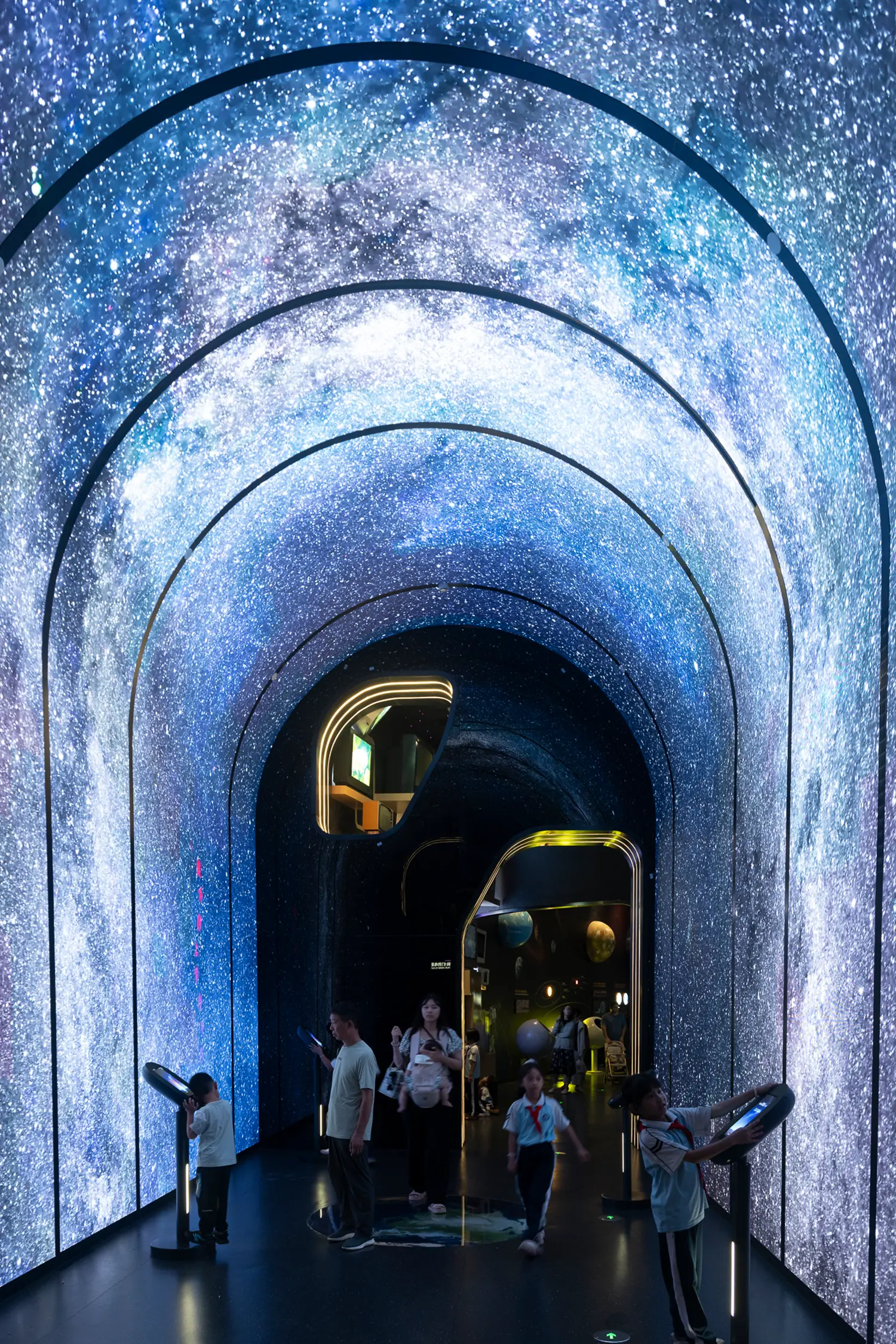 Visitors walking through an arched digital tunnel showing a high-resolution star-filled galaxy.