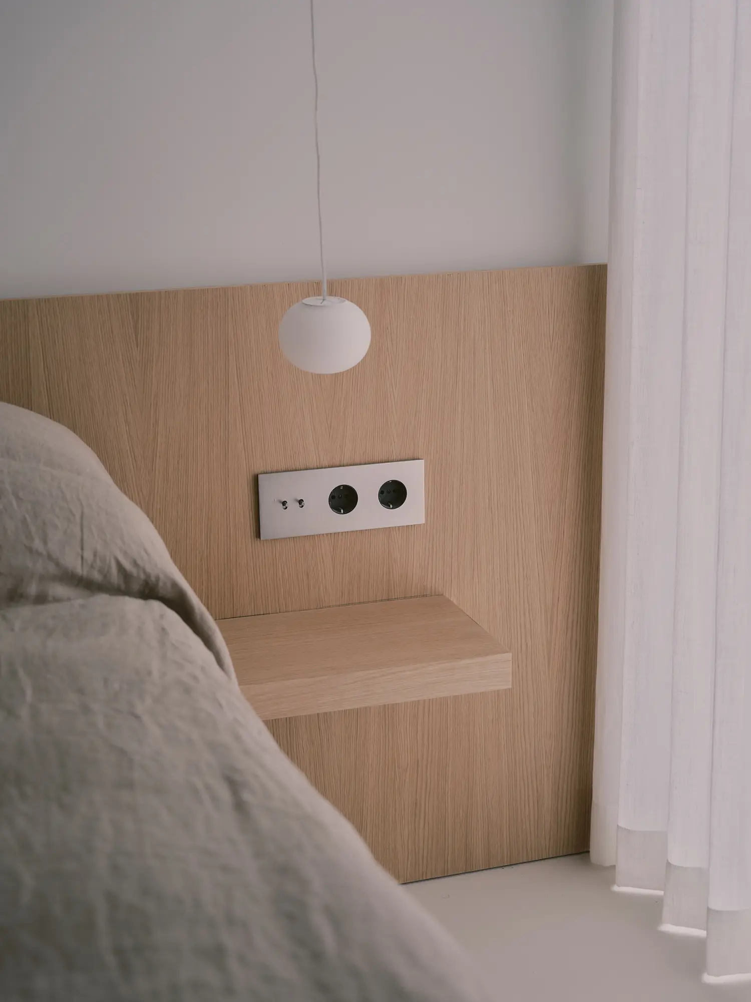 Detail of a bedroom with an oak headboard, integrated nightstand, and orb pendant light.