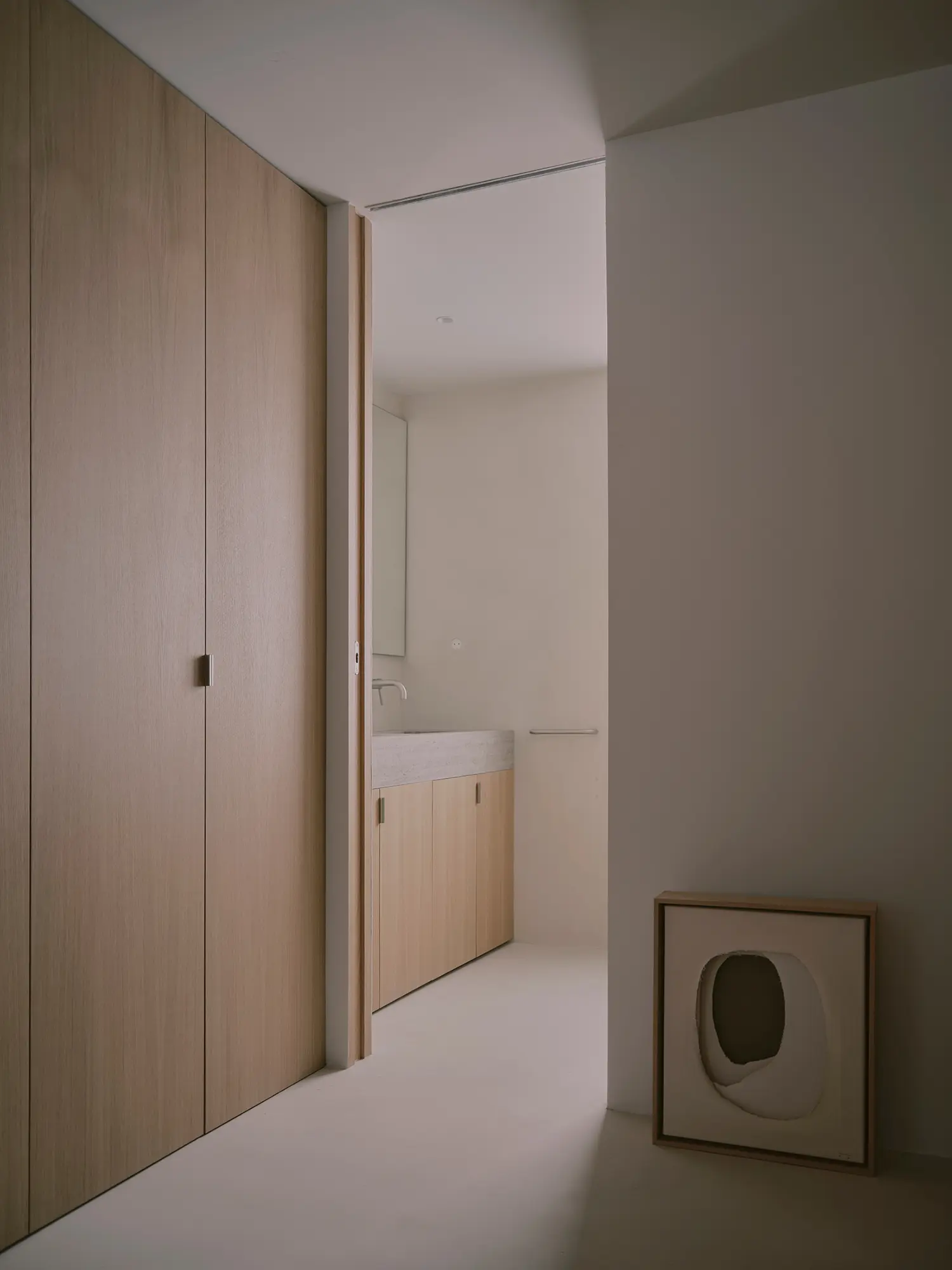 Minimalist hallway with oak wardrobes and a view into a stone-finished bathroom.