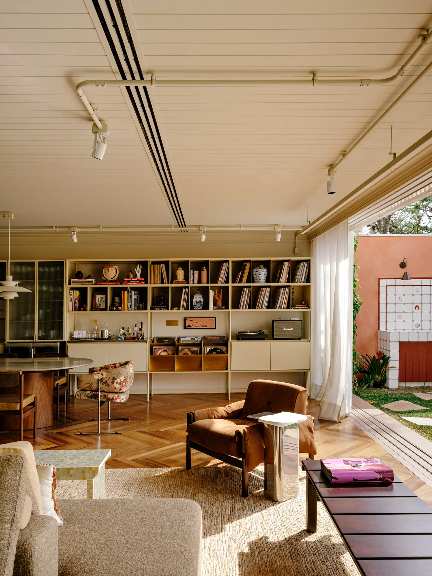 Mid-century armchairs and a dining table next to a modular metal shelving system under an exposed conduit ceiling.
