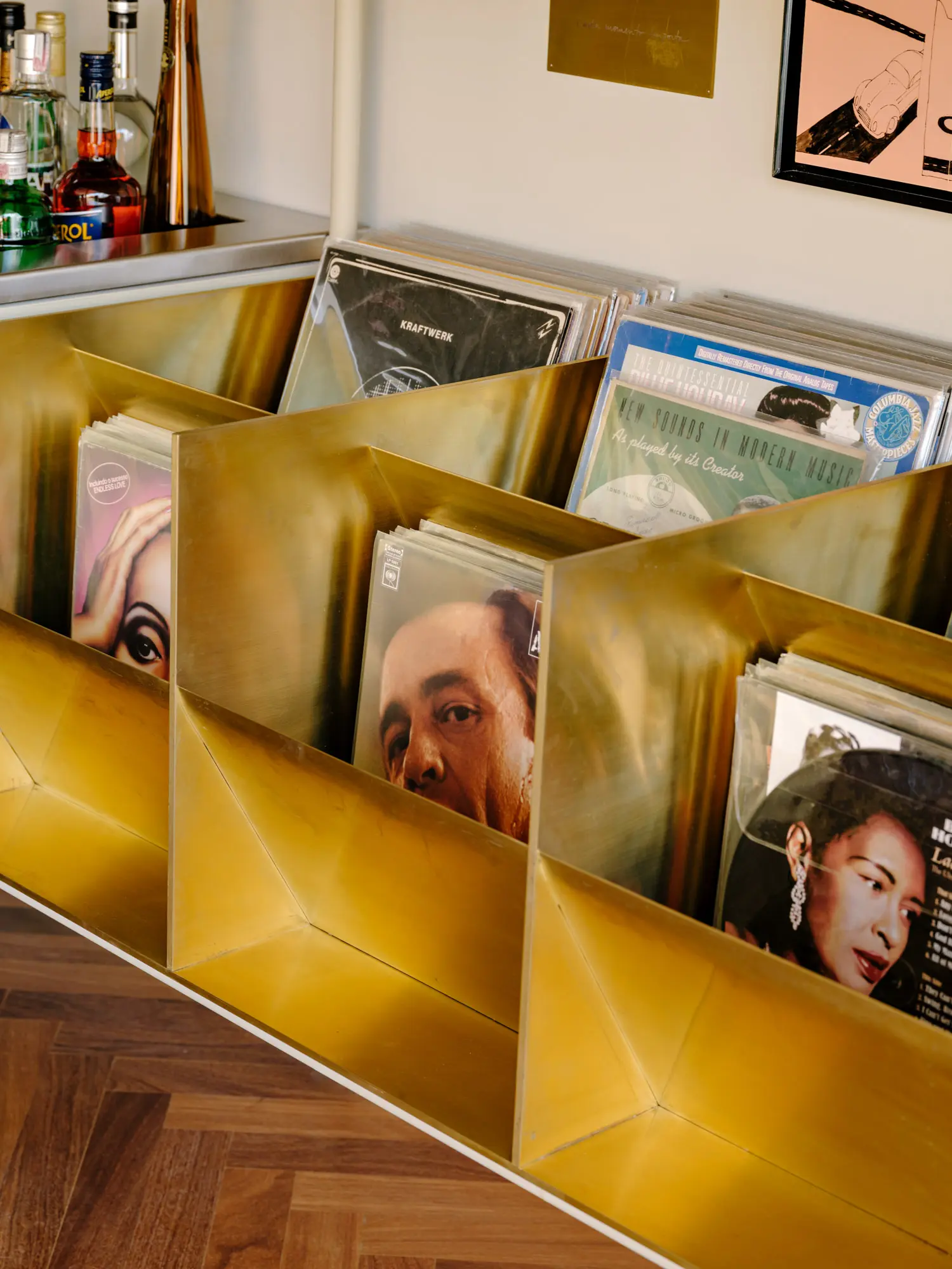 Close-up of vinyl record covers arranged inside a custom brass geometric shelving unit over a wood floor.