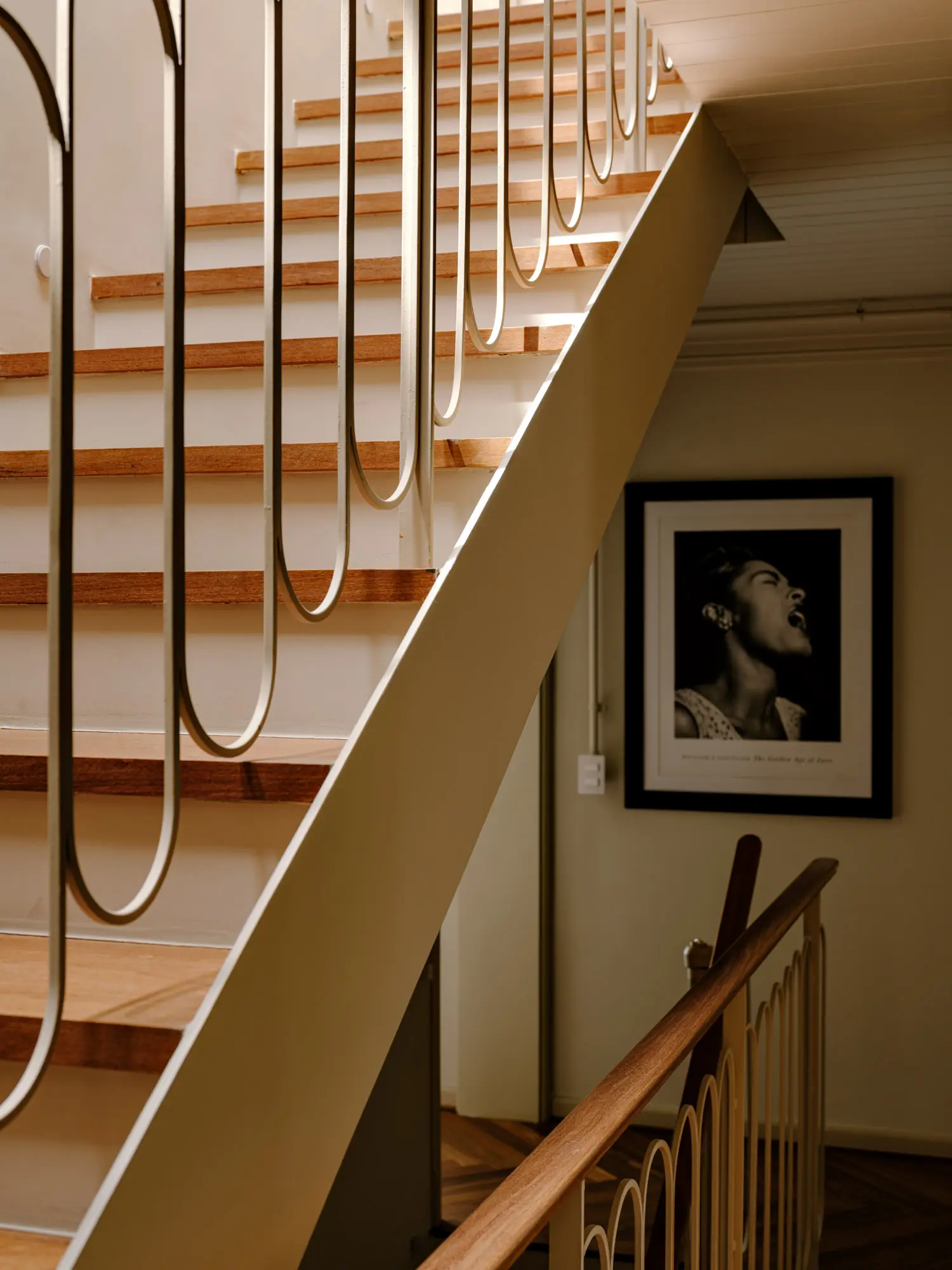 Detail of a staircase with light wood treads and curved metal guardrails next to a framed black-and-white portrait.