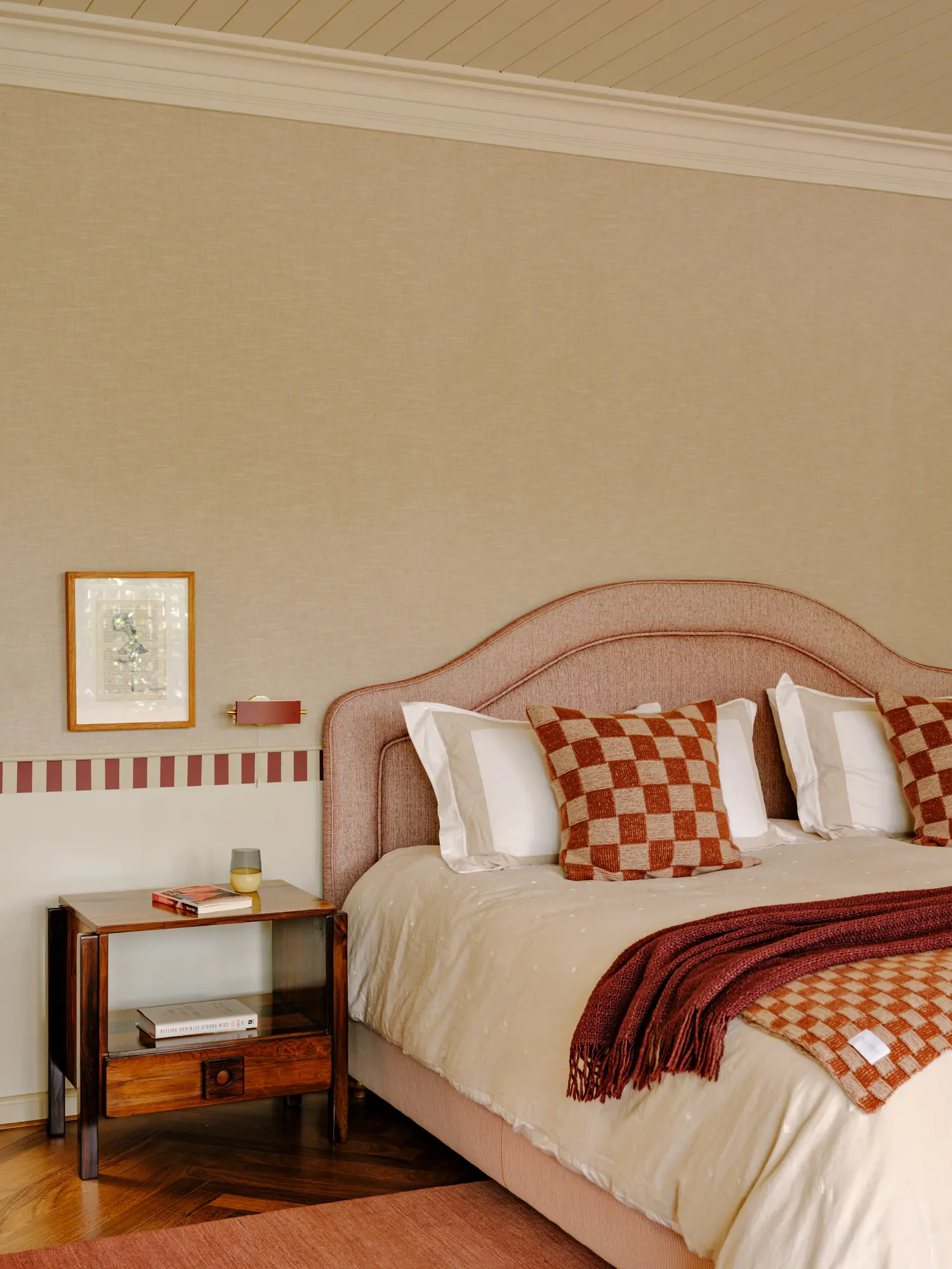 Bedroom with a salmon upholstered headboard, checkered pillows, a wooden nightstand, and striped wall tiles.