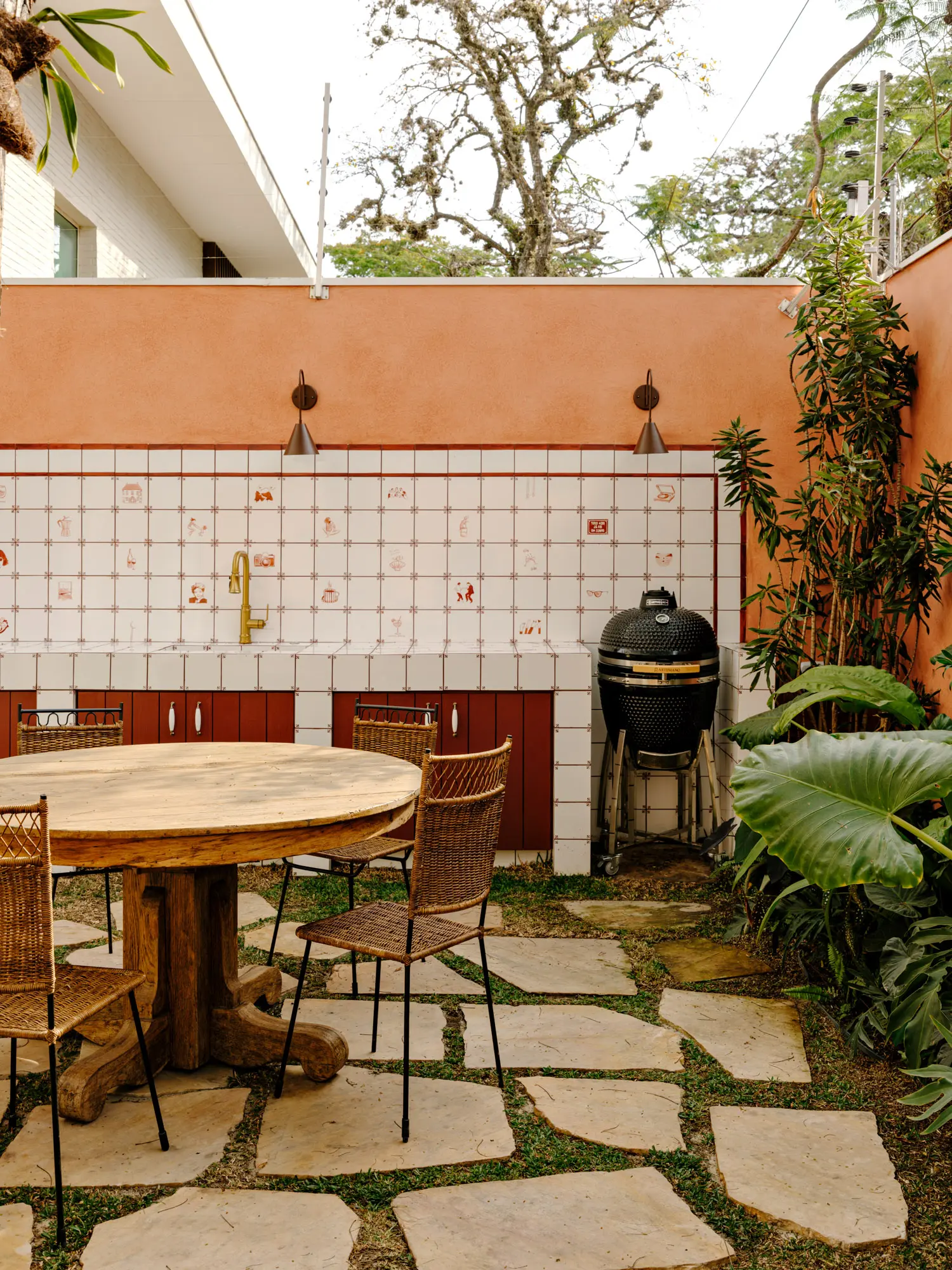 Outdoor courtyard with a rustic wooden table, stone paving, a terracotta wall, and custom white and red tiles.