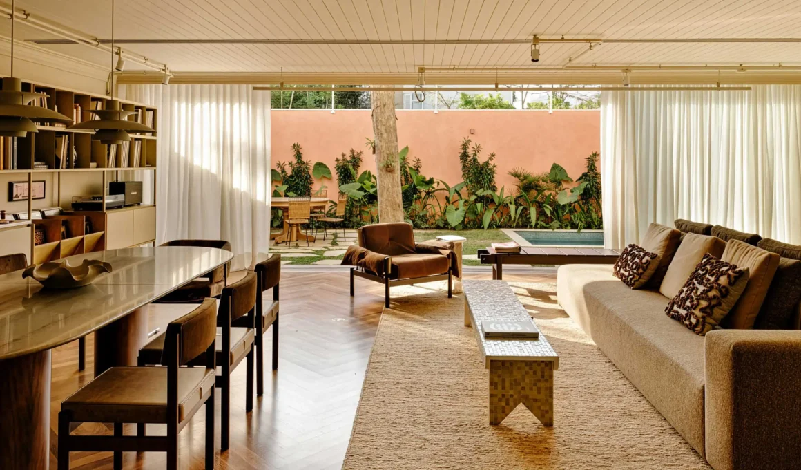 Open living room with herringbone wood floor, island sofa, beige ceiling, and wide open doors to a courtyard pool.