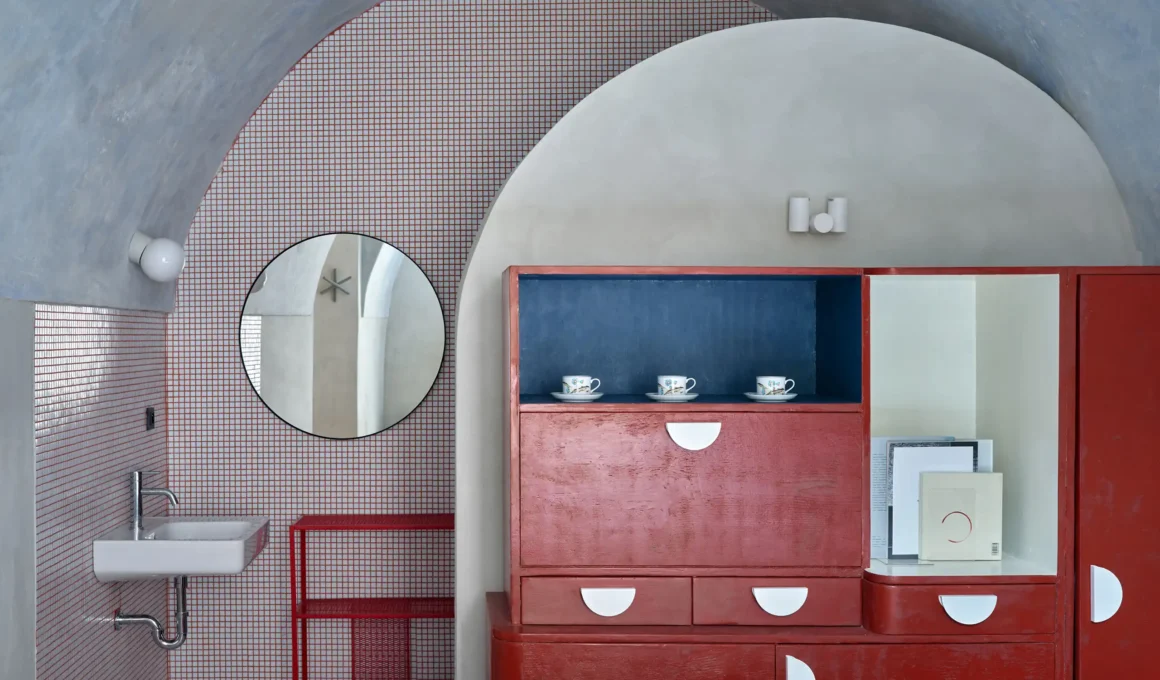 Oblouková 171 ORA — rebuilt barrel vault with lime plaster finish, red lacquered cabinet, small-grid mosaic tile bathroom beyond arch