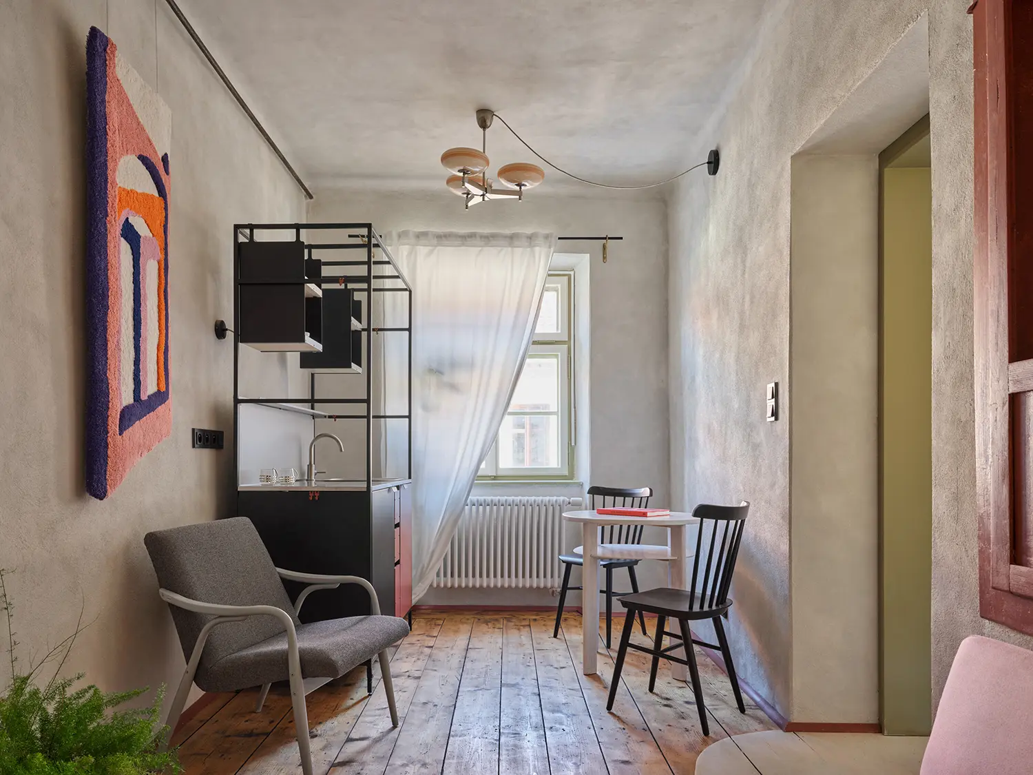 Oblouková 171 ORA — holiday apartment living area with original solid-plank timber floor, hand-applied plaster walls, modular black steel kitchen unit