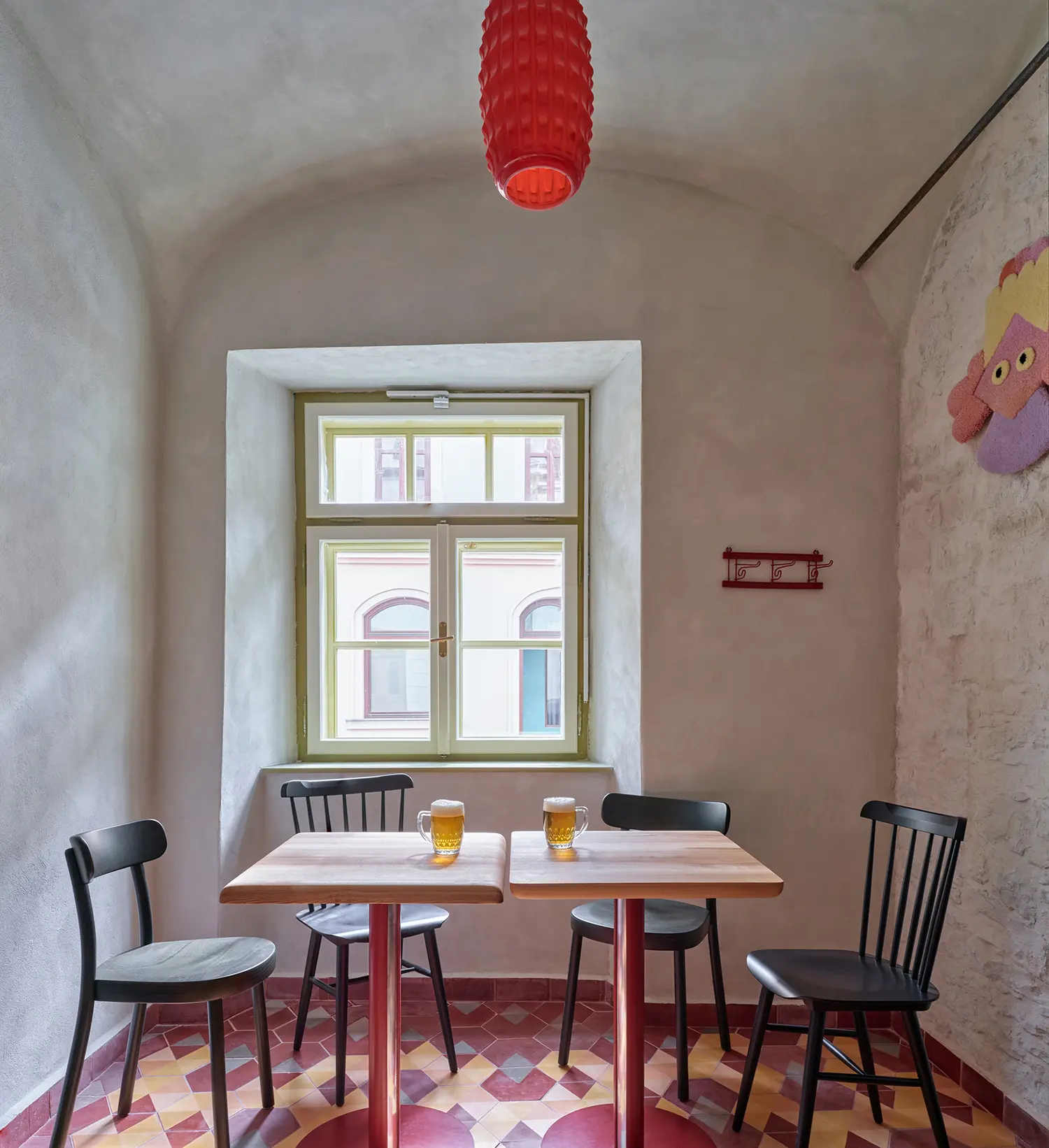 Oblouková 171 ORA — taproom corner with salvaged geometric floor tiles, lime-plastered barrel vault, olive-green window frame, red glass pendant light