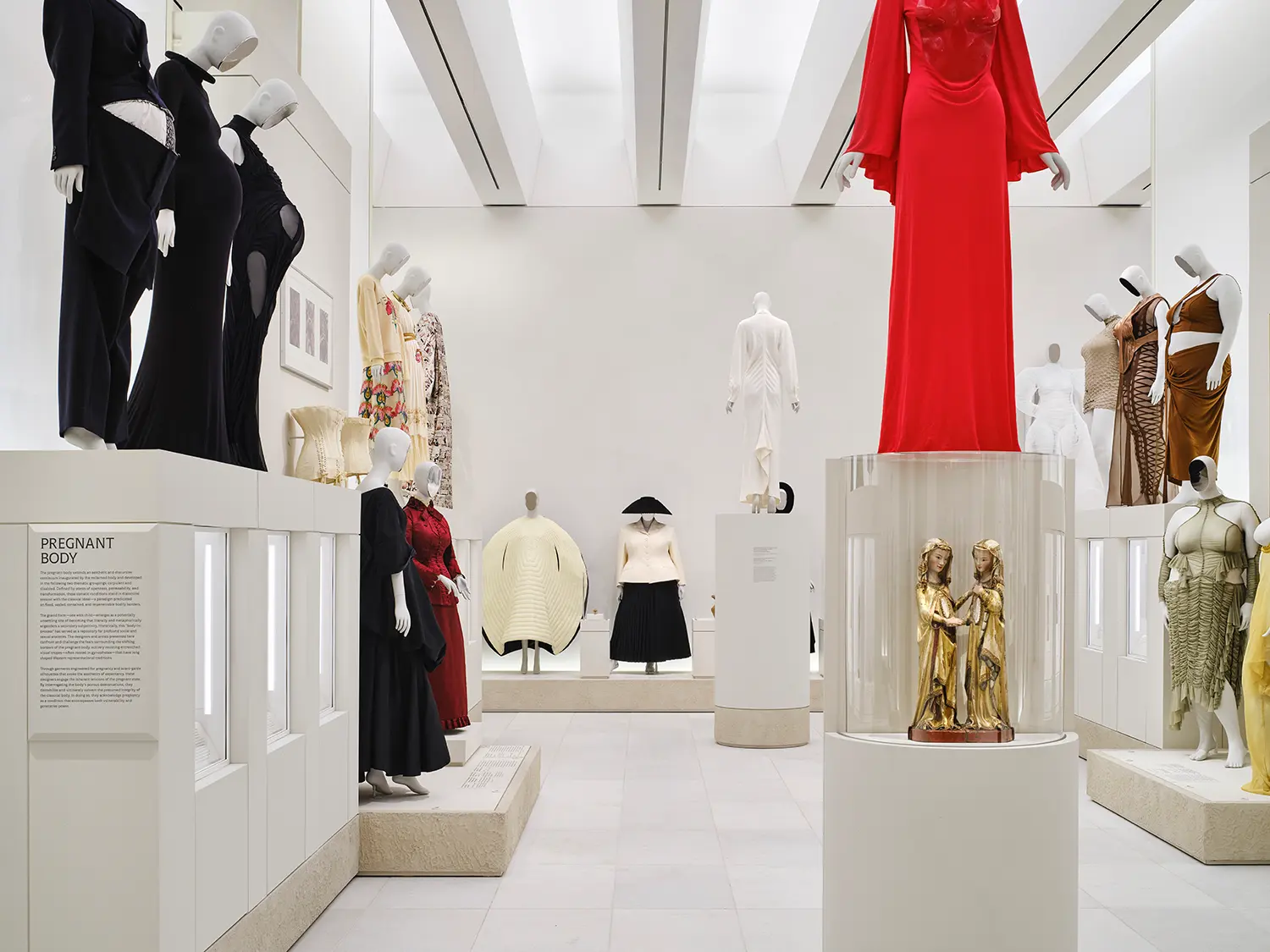 High-ceiling gallery showing contemporary fashion pieces on display platforms in front of a monumental exposed historic brick wall.