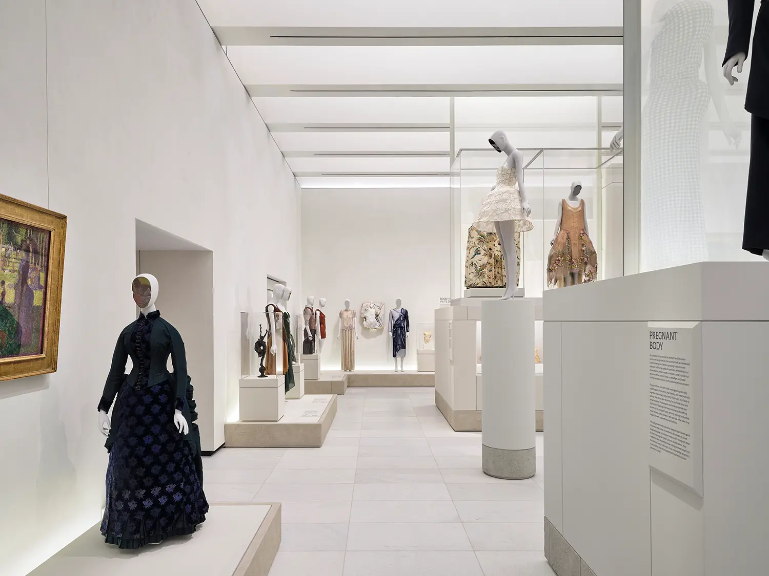 Expansive gallery hall with historic red brick walls on one side and smooth white walls on the other, displaying mannequins on raised platforms.