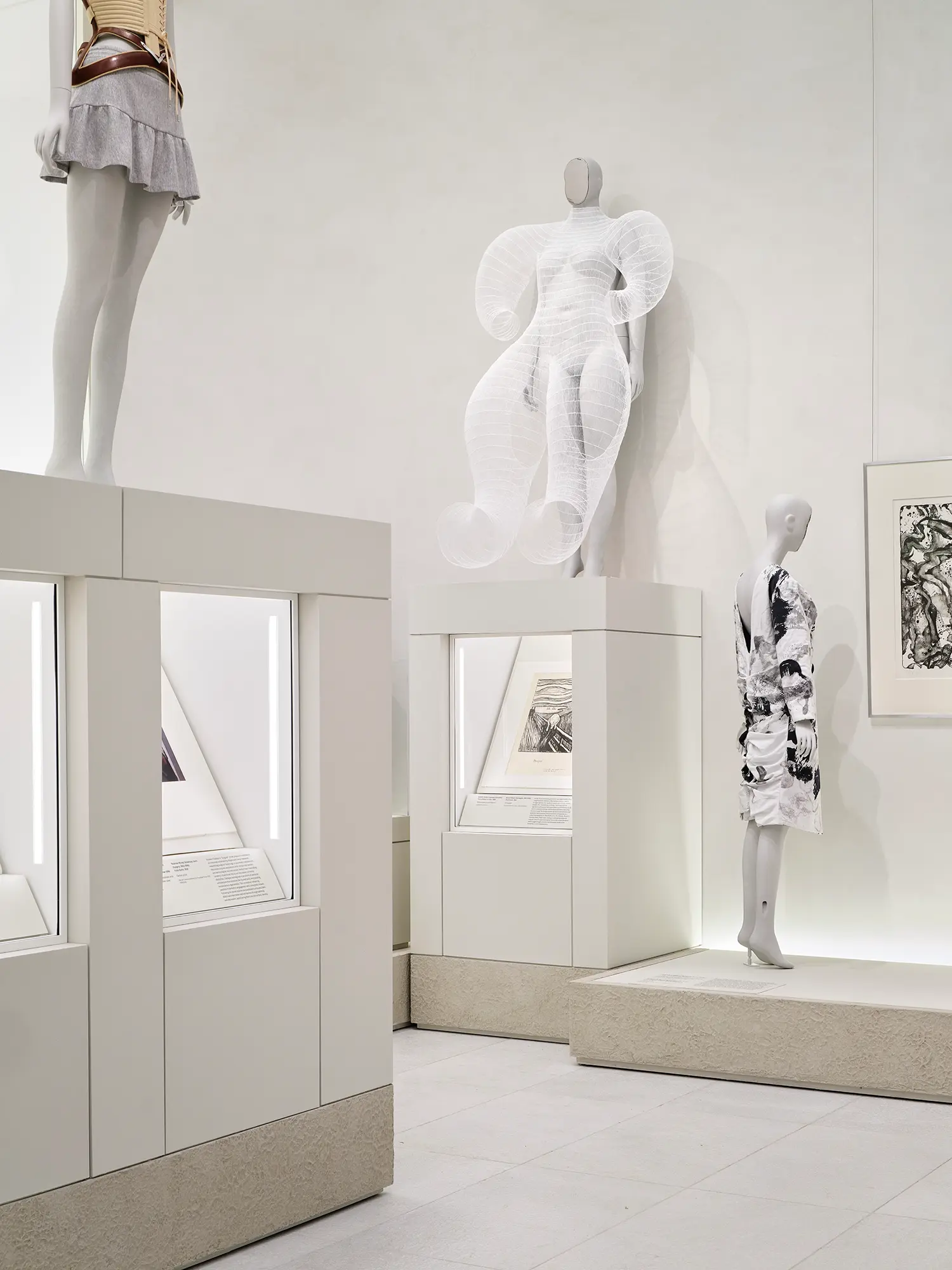 Intimate low-ceiling gallery with grey stone flooring displaying black and white avant-garde mannequins wearing dark textured fashion.