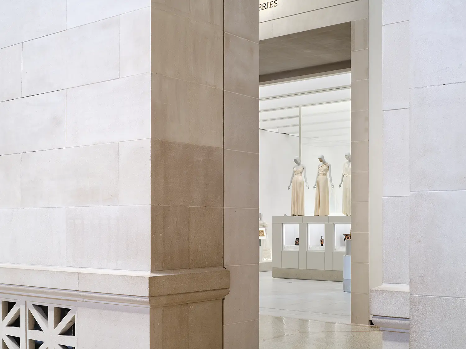 Corner of a contemporary museum gallery showing a historic brick wall meeting a smooth white plaster wall beneath modern gallery lighting.