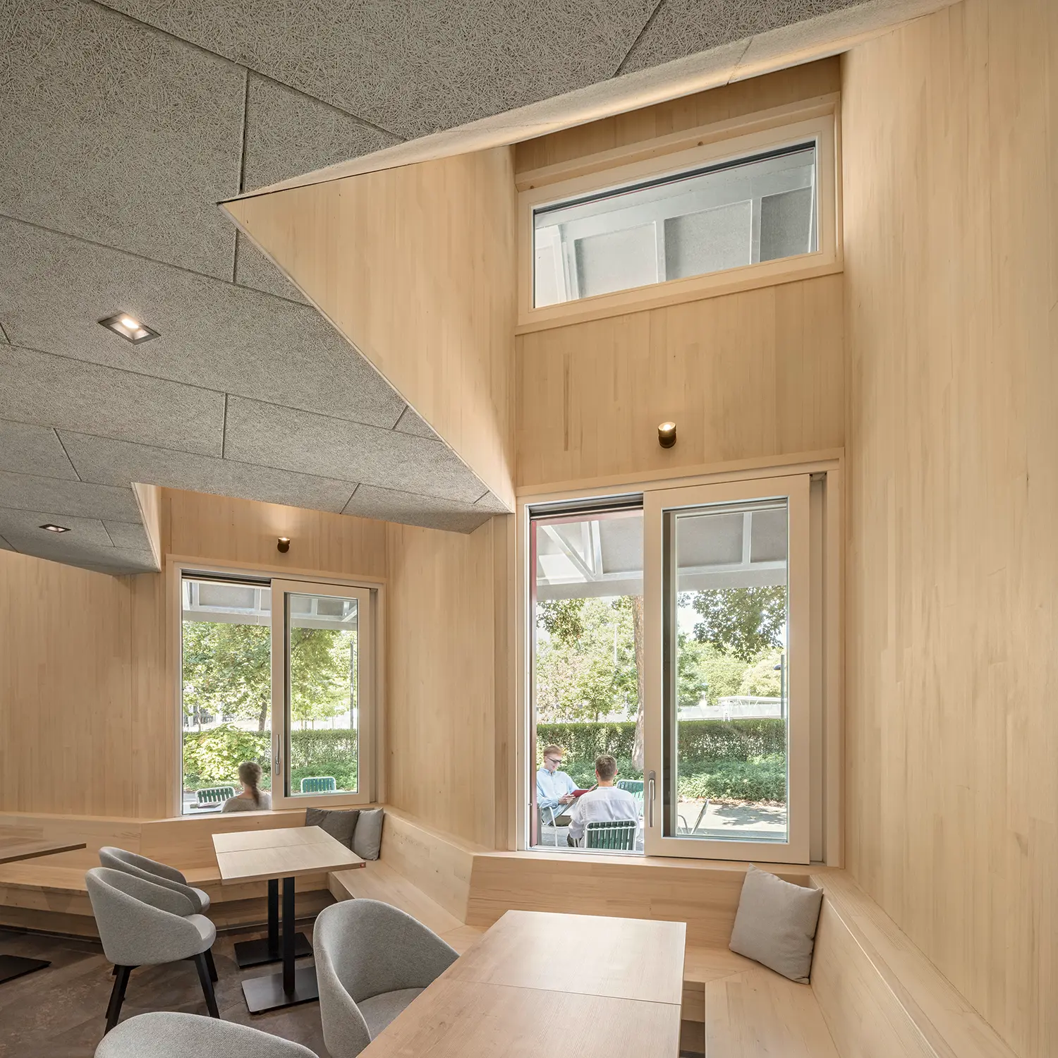 Interior view of a wooden dining niche at Café Restaurant Resselpark with silver fir cladding and large windows.