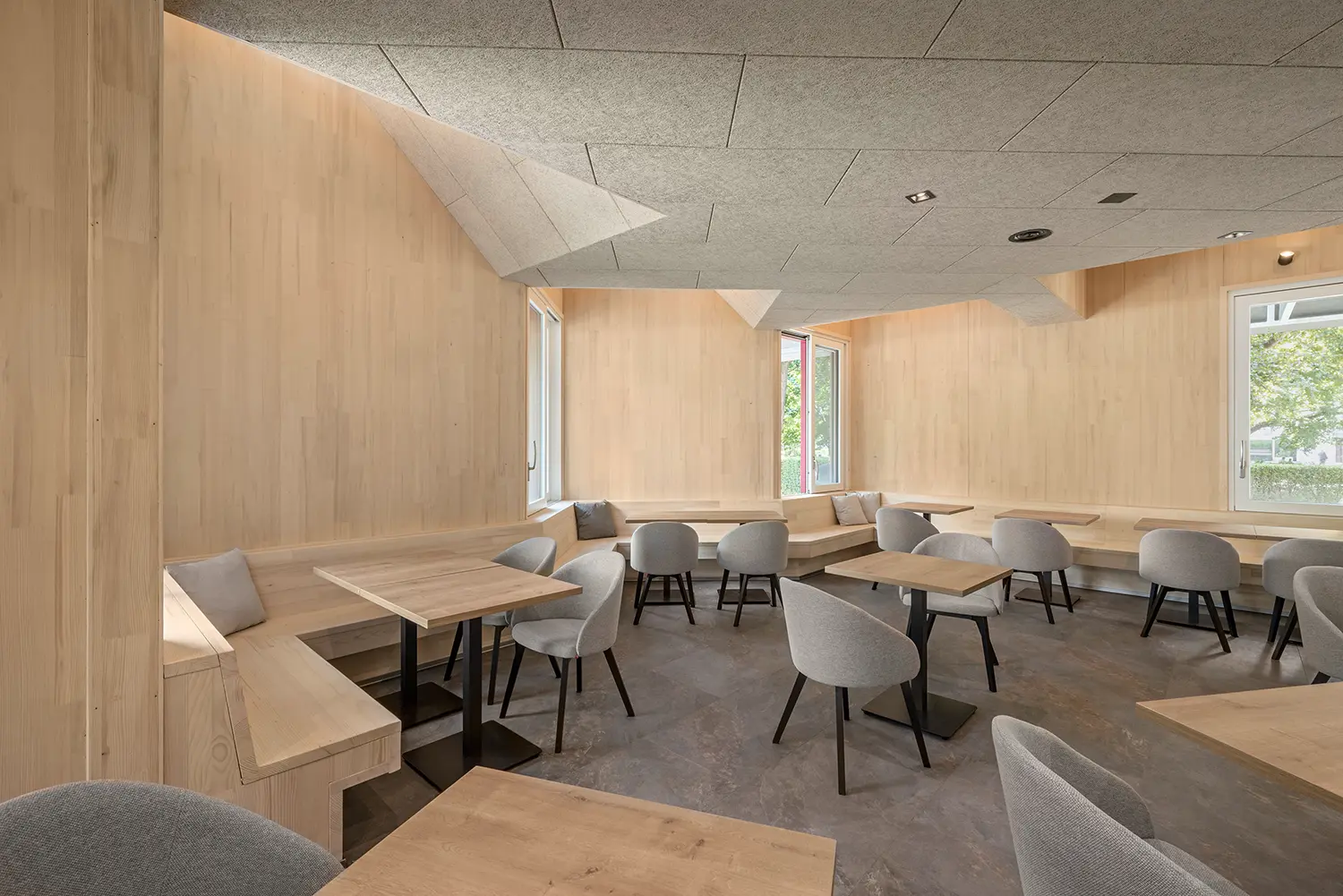 Minimalist interior of the Resselpark dining area featuring CLT walls and gray upholstered seating.