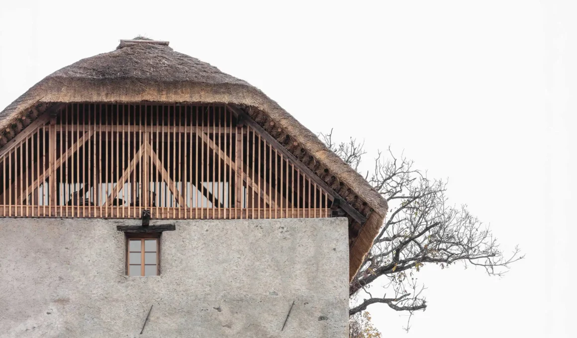 Close-up of a historic Alpine barn featuring a thatched roof and vertical timber slats over a textured plaster facade.