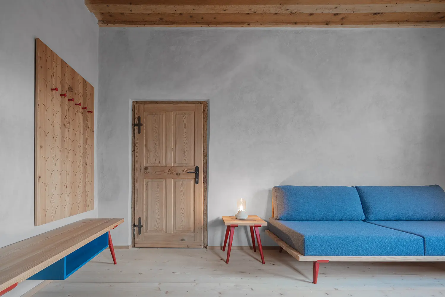 Minimalist living room with a blue sofa, light wood floors, and a historic timber door against a grey lime-wash wall.
