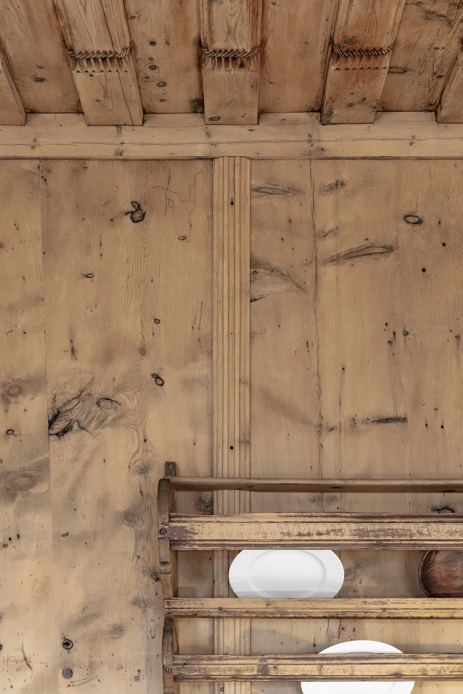 Close-up of aged vertical wood paneling with visible knots and a rustic wooden shelf holding a white plate.