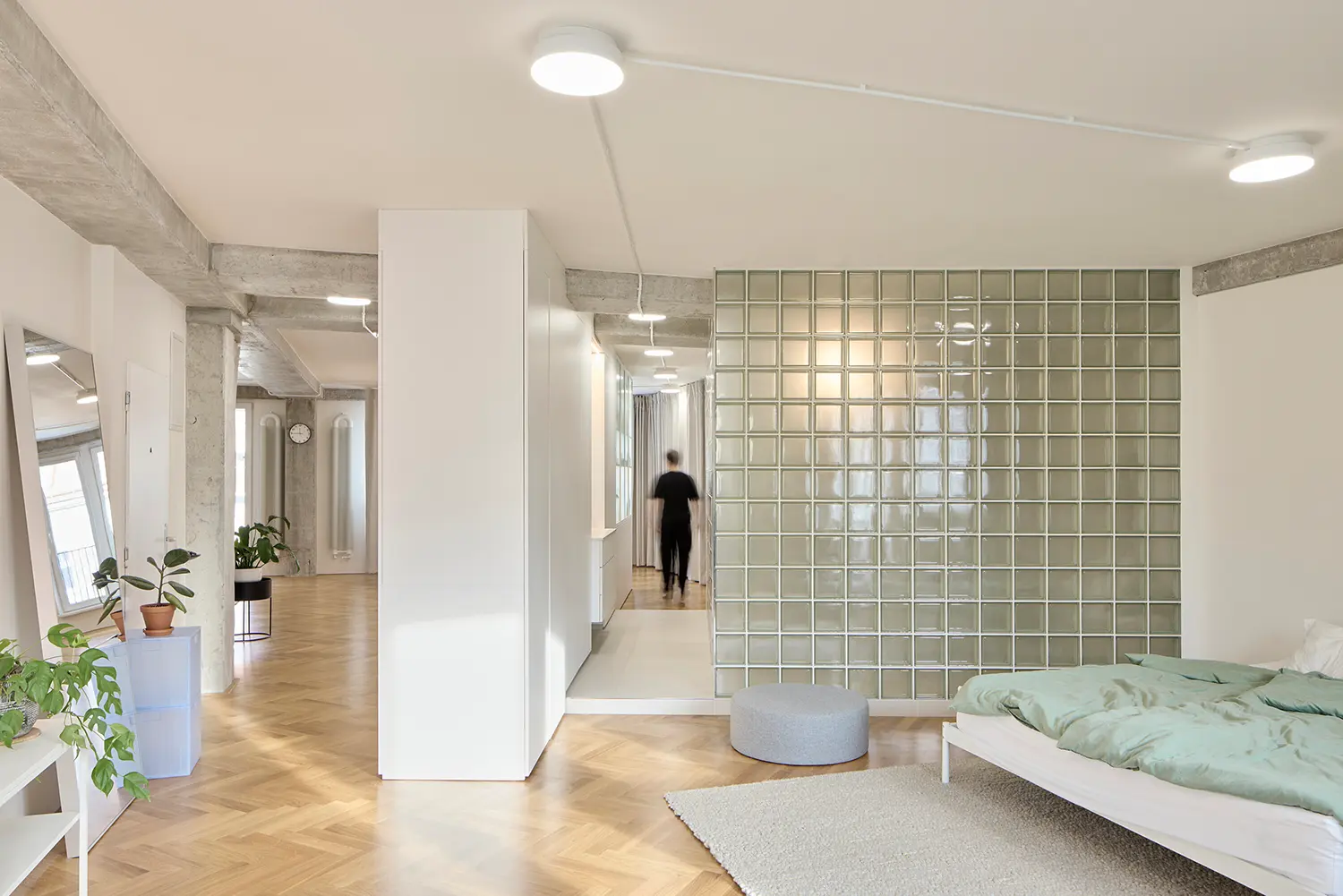 A spacious bedroom with a green-bedded white frame next to a large square wall of green translucent glass blocks.