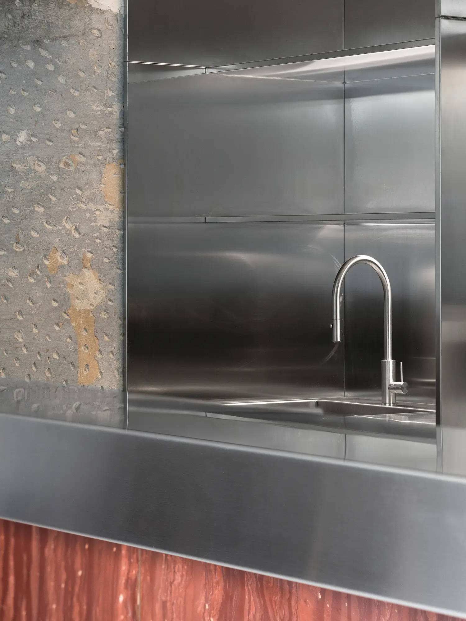 Close-up of a stainless steel sink and backsplash against a raw, chiseled masonry wall.