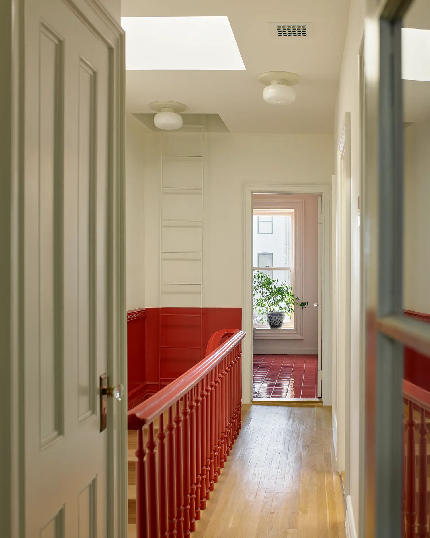 Hallway with a red-painted banister and wainscoting leading toward a room with a red-tiled floor.