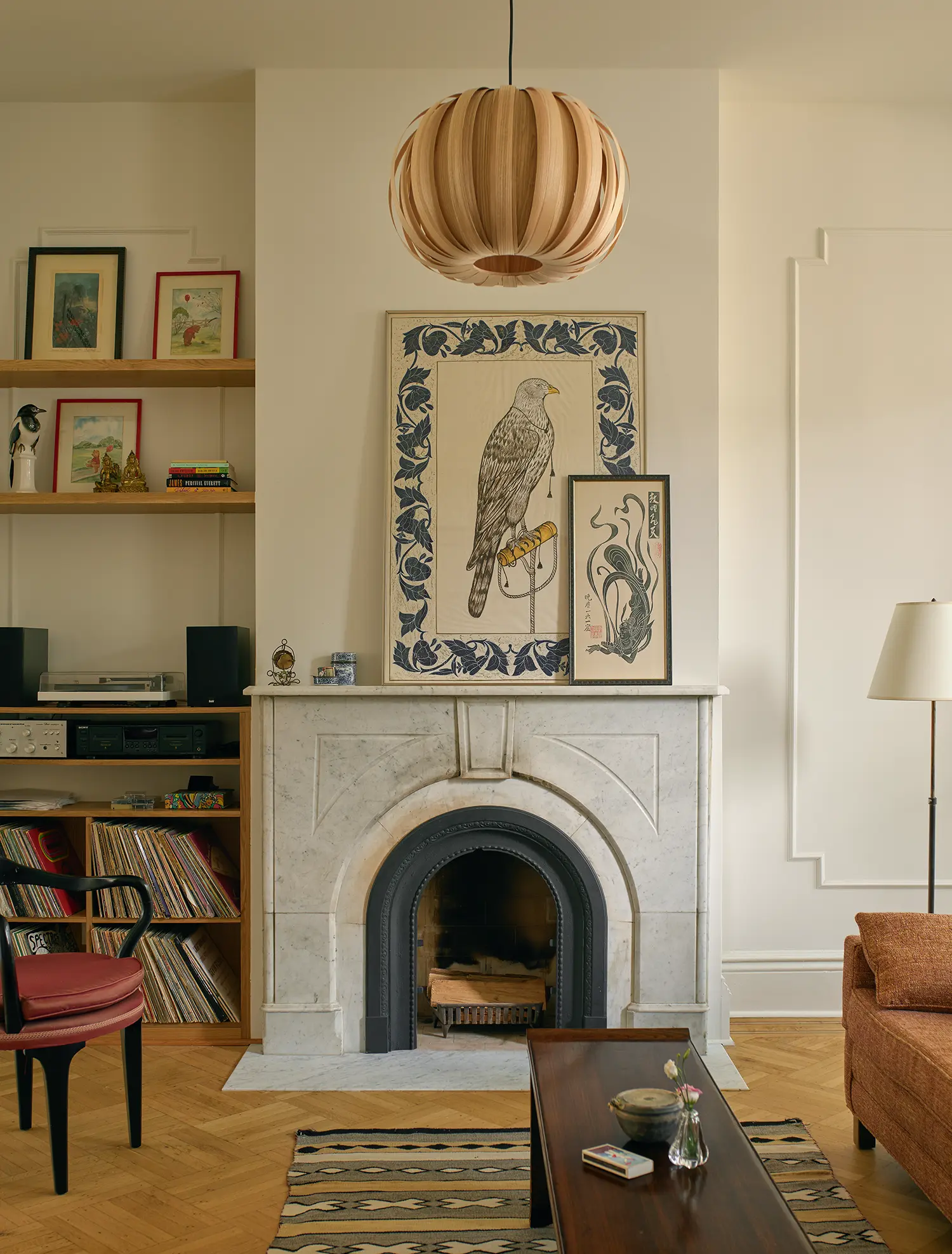 Ornate white marble fireplace with a bird illustration on the mantle, flanked by bookshelves and a wooden pendant light.