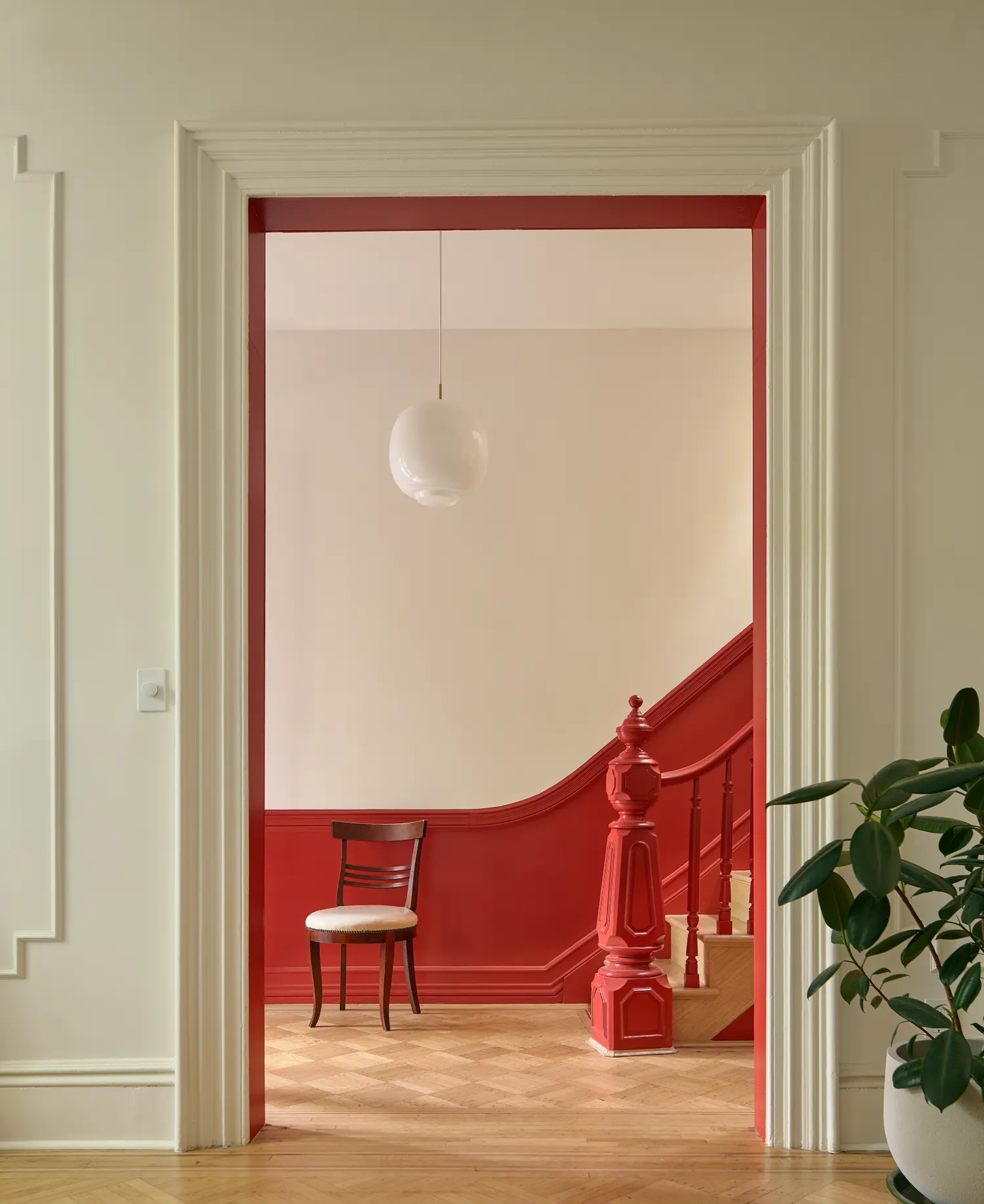A doorway with a bold red frame leading to a staircase with matching red banisters and wainscoting.