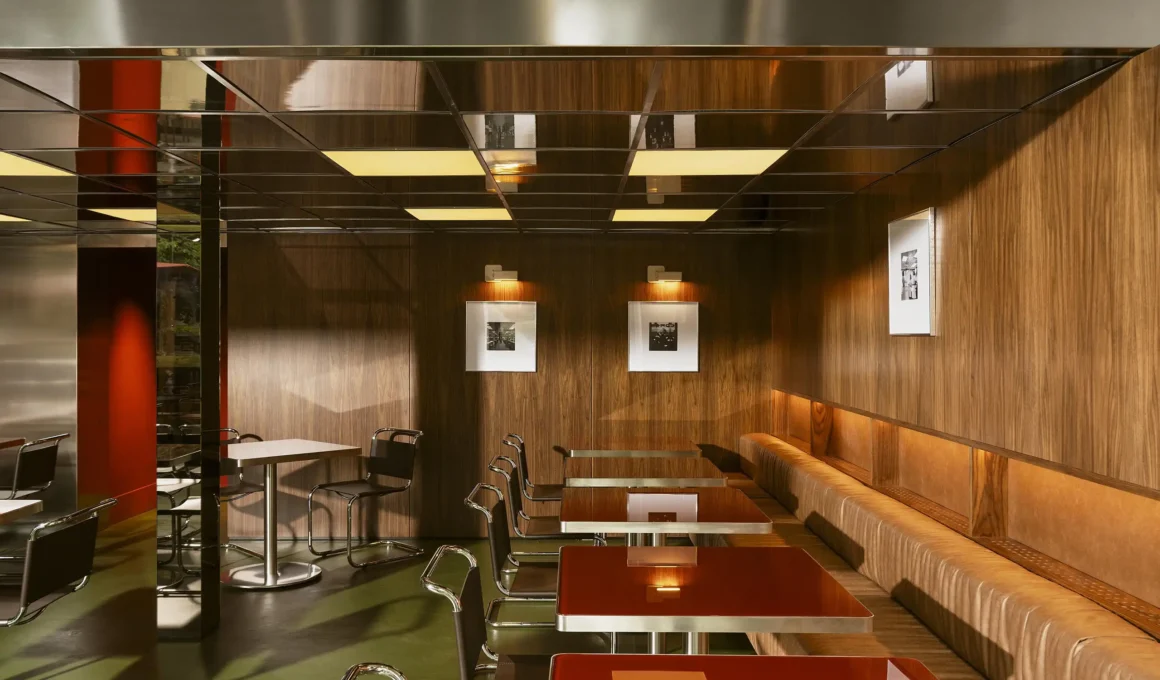 A seating area in Lève Office Bar with wood-paneled walls, glossy red tables, and a reflective gridded ceiling.