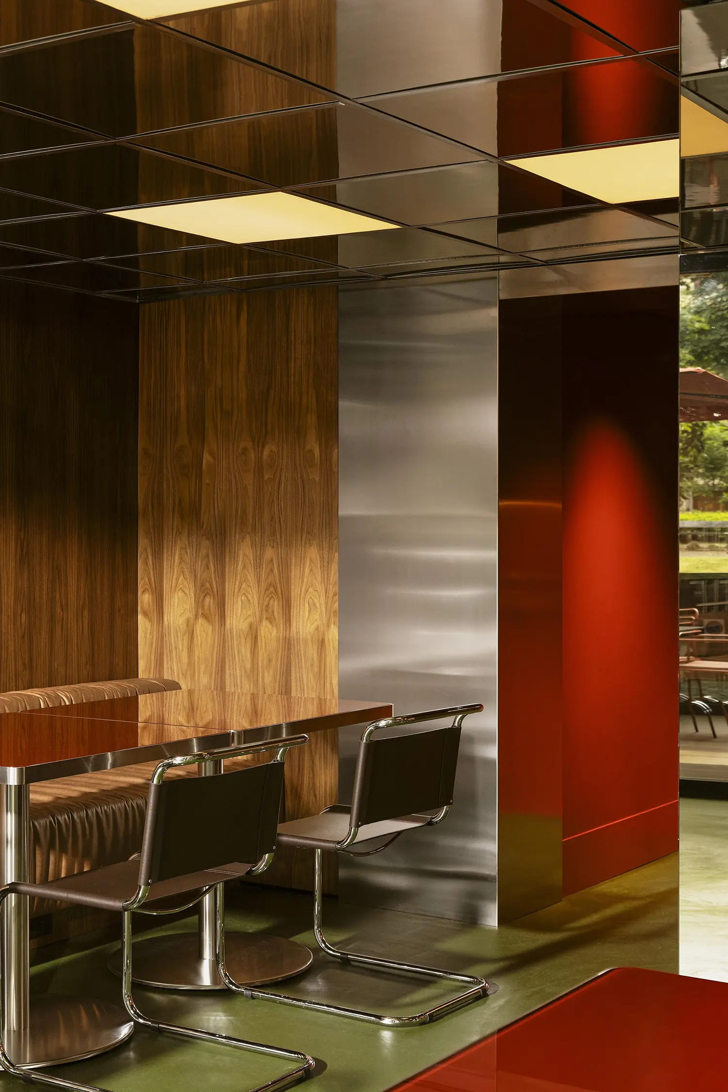 A dining vignette featuring a mirrored ceiling, chrome chairs, and an accent wall in deep red enamel.