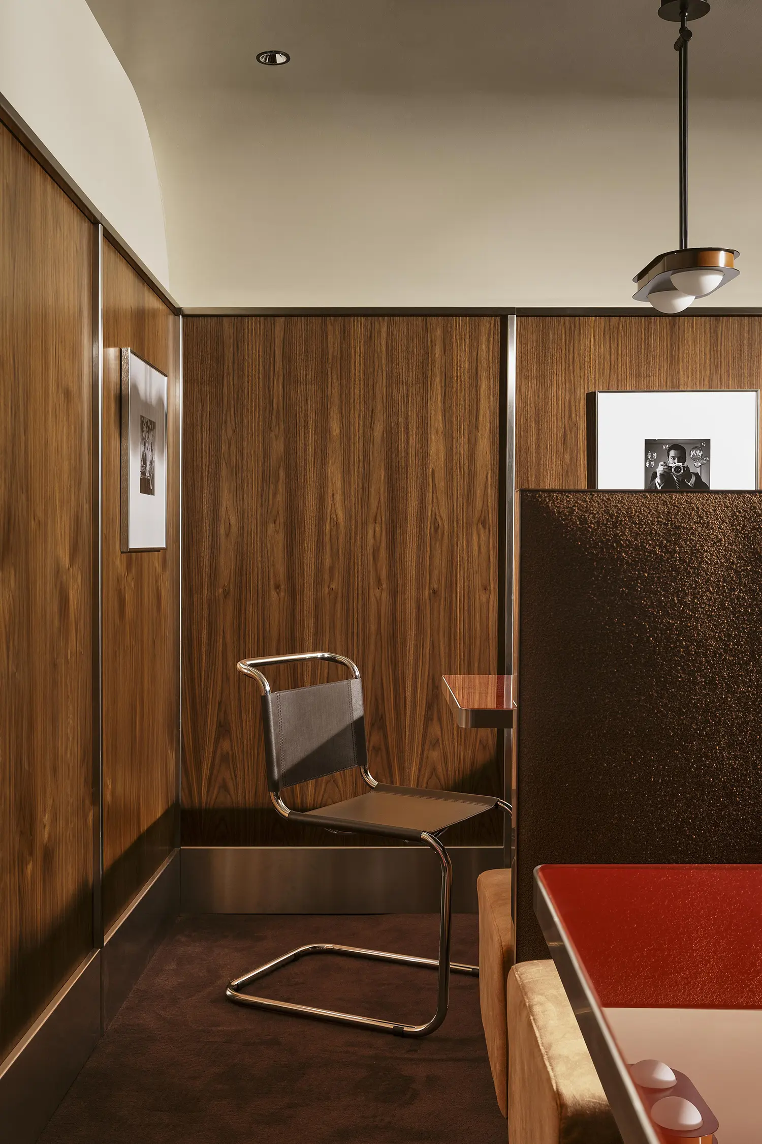 A single mid-century chrome cantilever chair positioned against rich walnut boiserie.