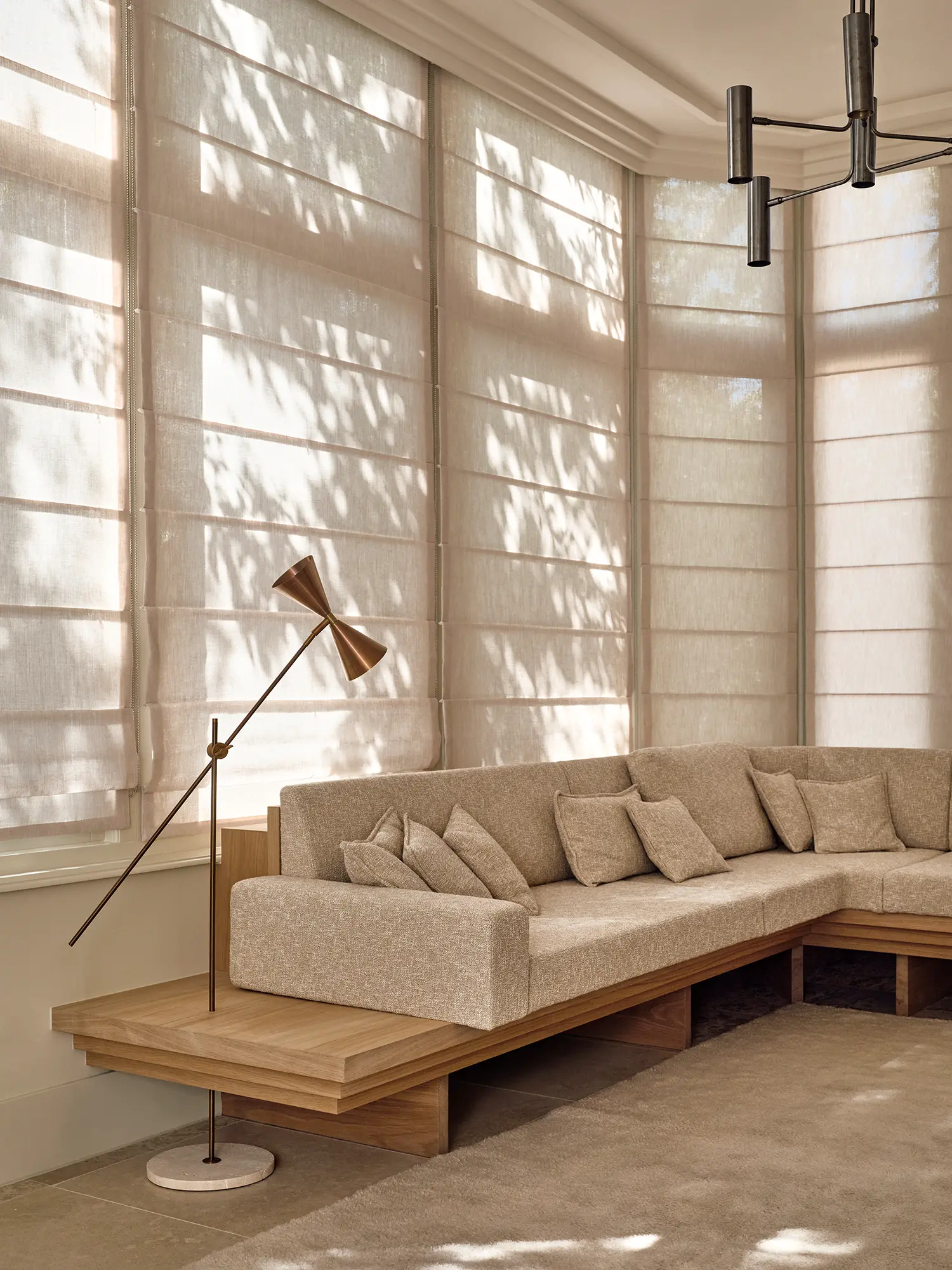 Serre living area with custom oak-framed sofa, linen Roman blinds, brass floor lamp and filtered natural light