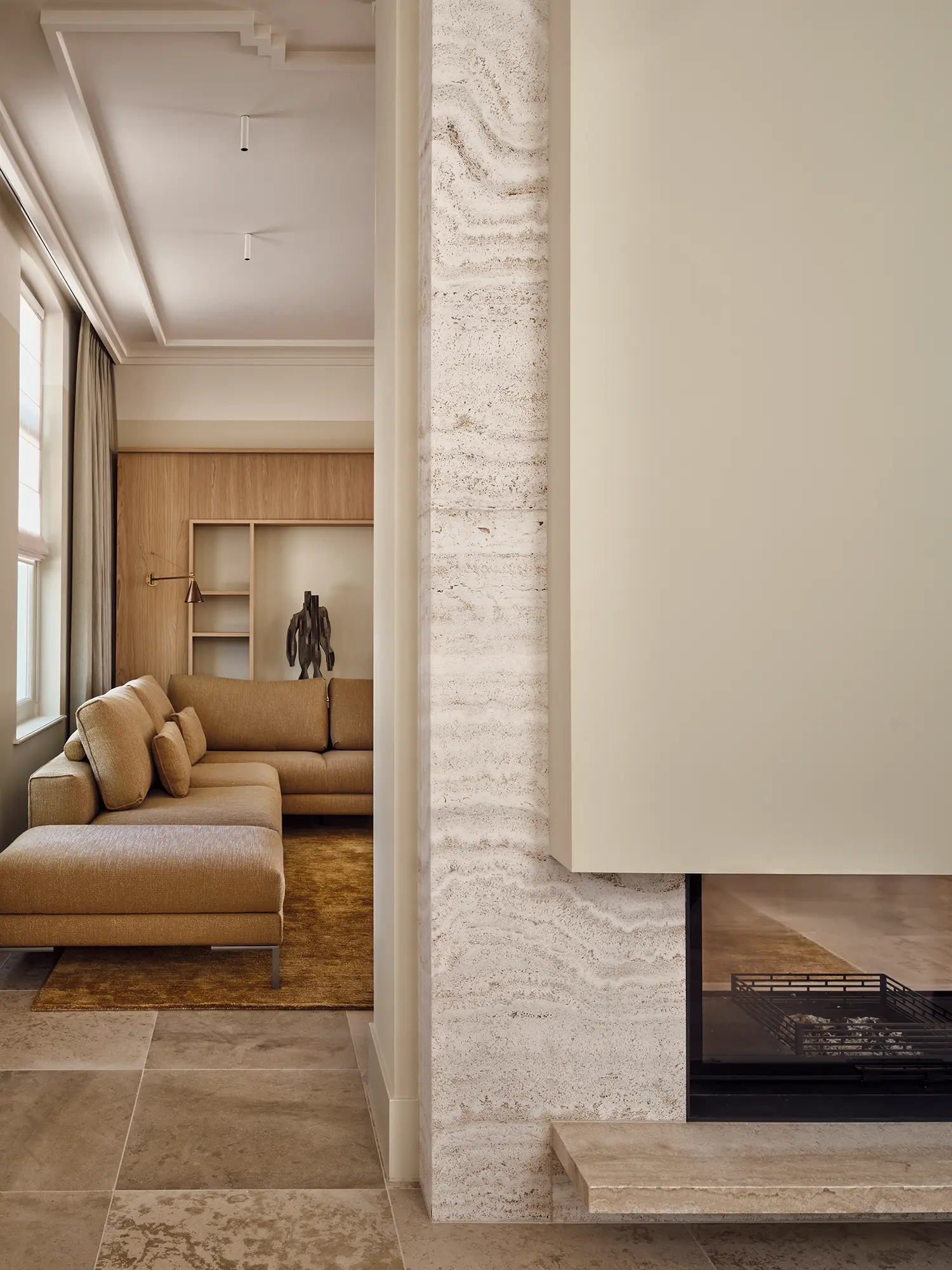 Travertine fireplace surround with view into living room featuring sculptural artwork, golden rug and walnut cabinetry