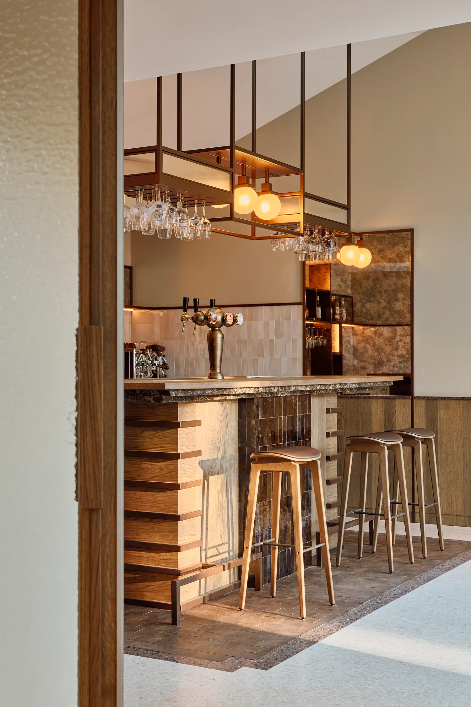ome bar with brass overhead rack, Zellige tiles, antique mirror back wall, mixed bar stools and terrazzo floor