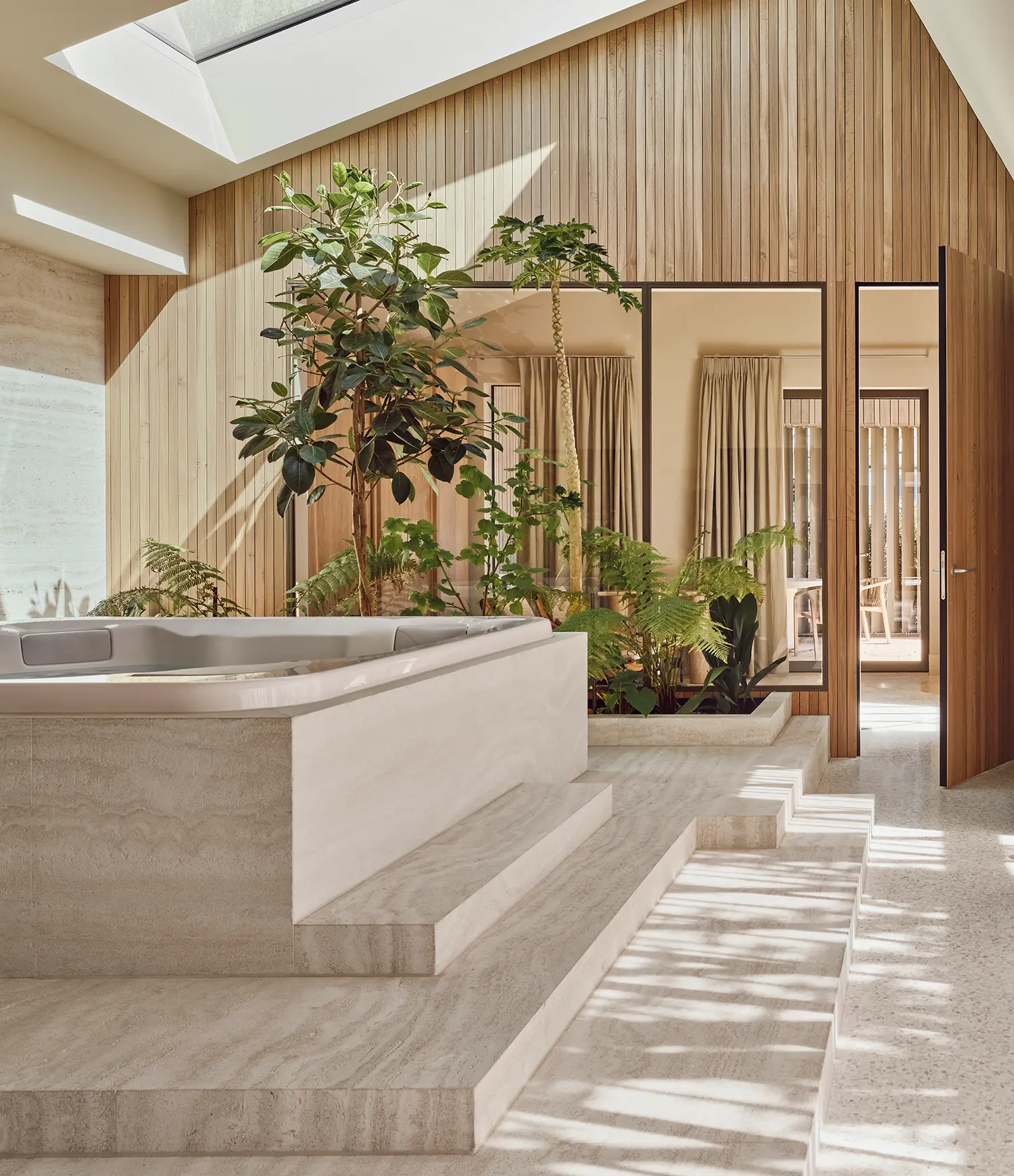 Wellness area with travertine-clad jacuzzi, vertical timber walls, skylight, tropical plants and terrazzo floor