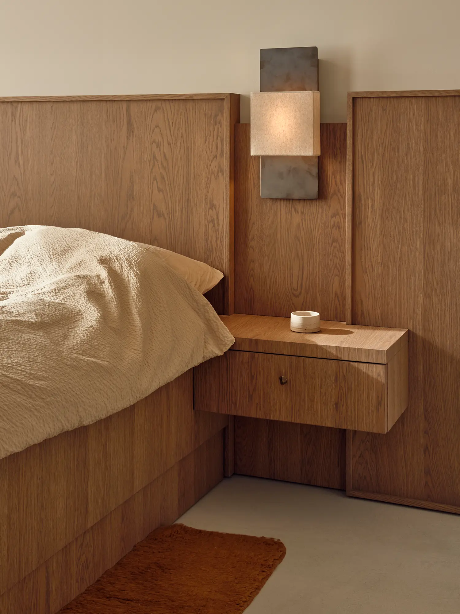 Master bedroom detail with custom oak headboard, integrated floating nightstand and stone-and-metal wall sconce