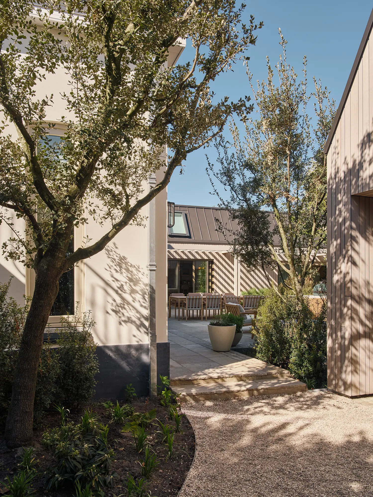 Exterior garden view between historic 1920s main house and new timber-clad extension with outdoor dining terrace