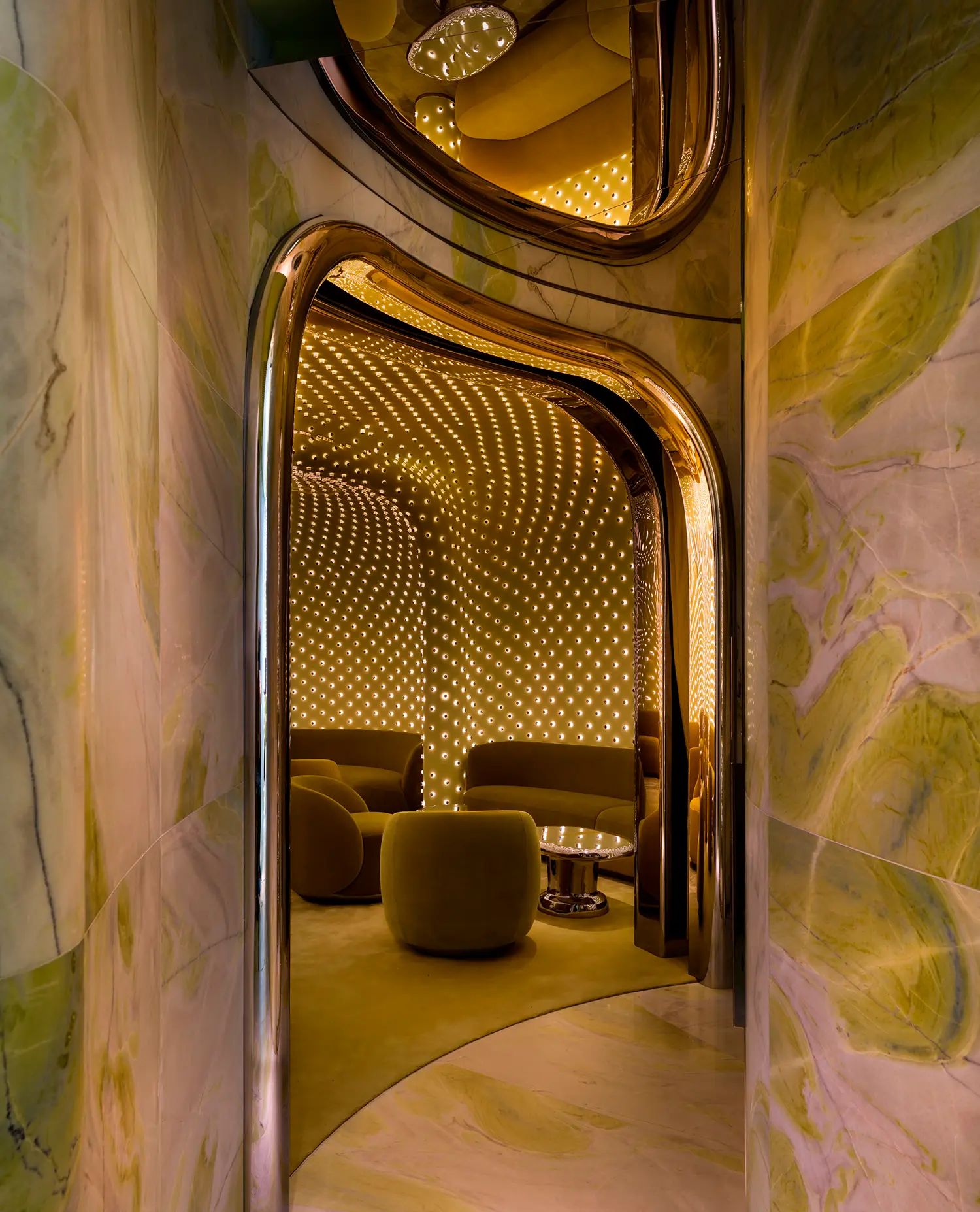 A polished gold arched doorway reflecting the green marble walls and the illuminated ceiling of the Peridot cocktail bar.
