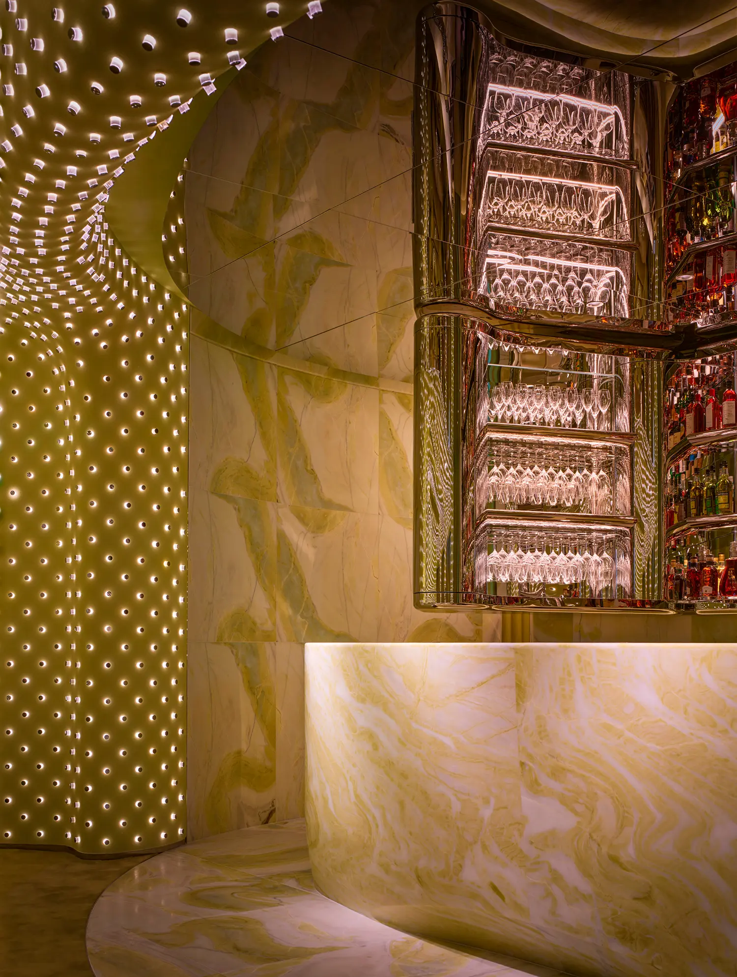 Close-up of a monumental green marble bar counter with a tiered back bar display and glowing light grid wall.
