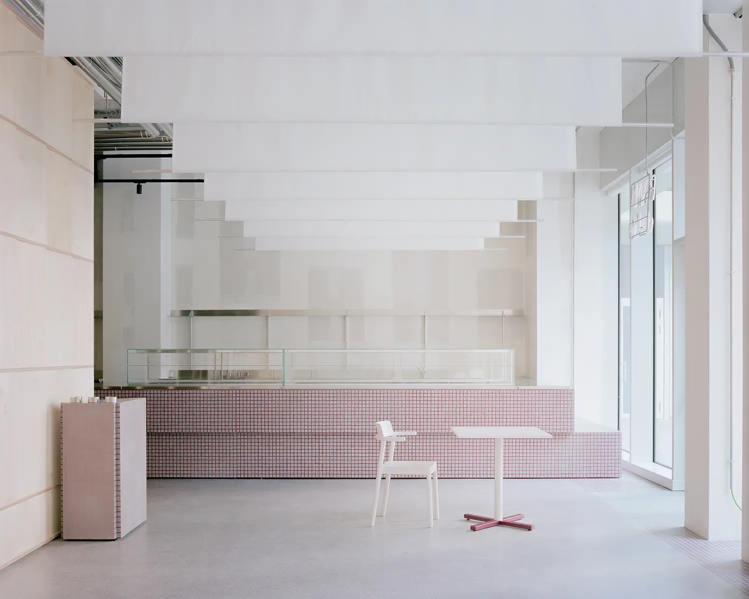 A long service counter clad in small pinkish-purple square gridded tiles beneath hanging white fabric ceiling panels in a minimalist Milan deli.