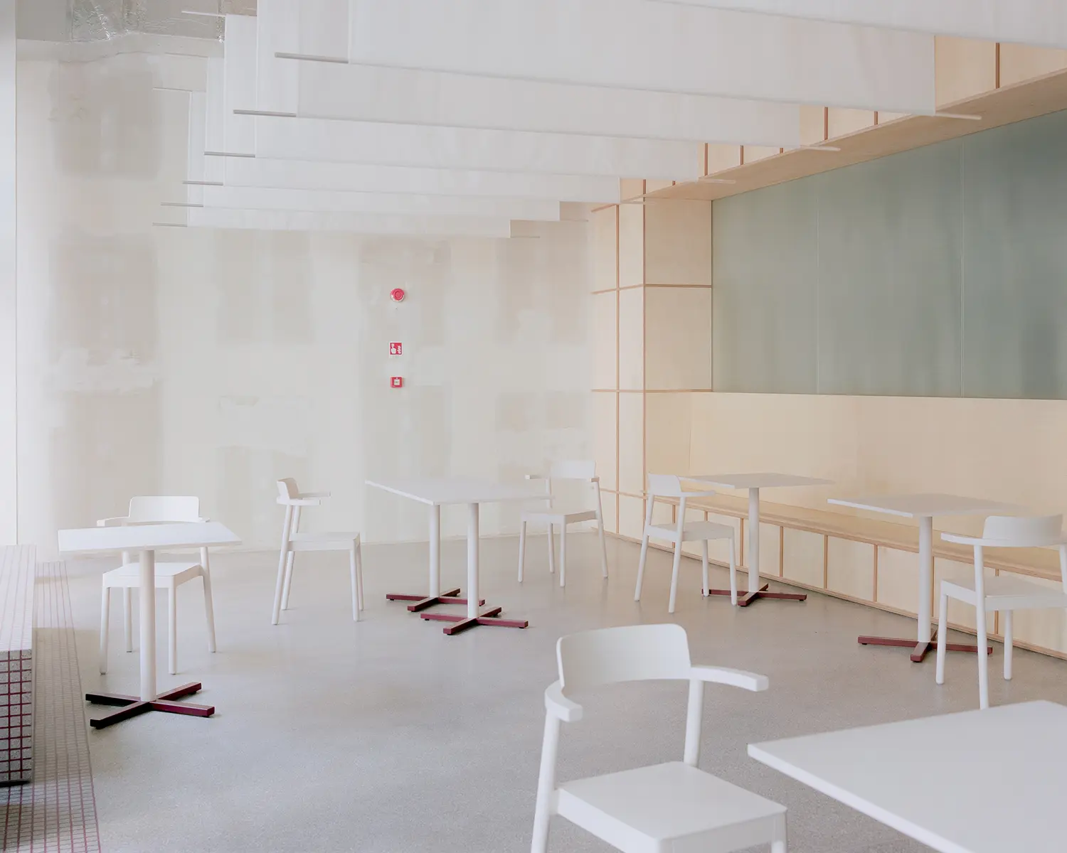 Minimalist white dining furniture arranged in a bright, open cafe dining area with raw unfinished plaster walls and hanging fabric ceiling baffles.