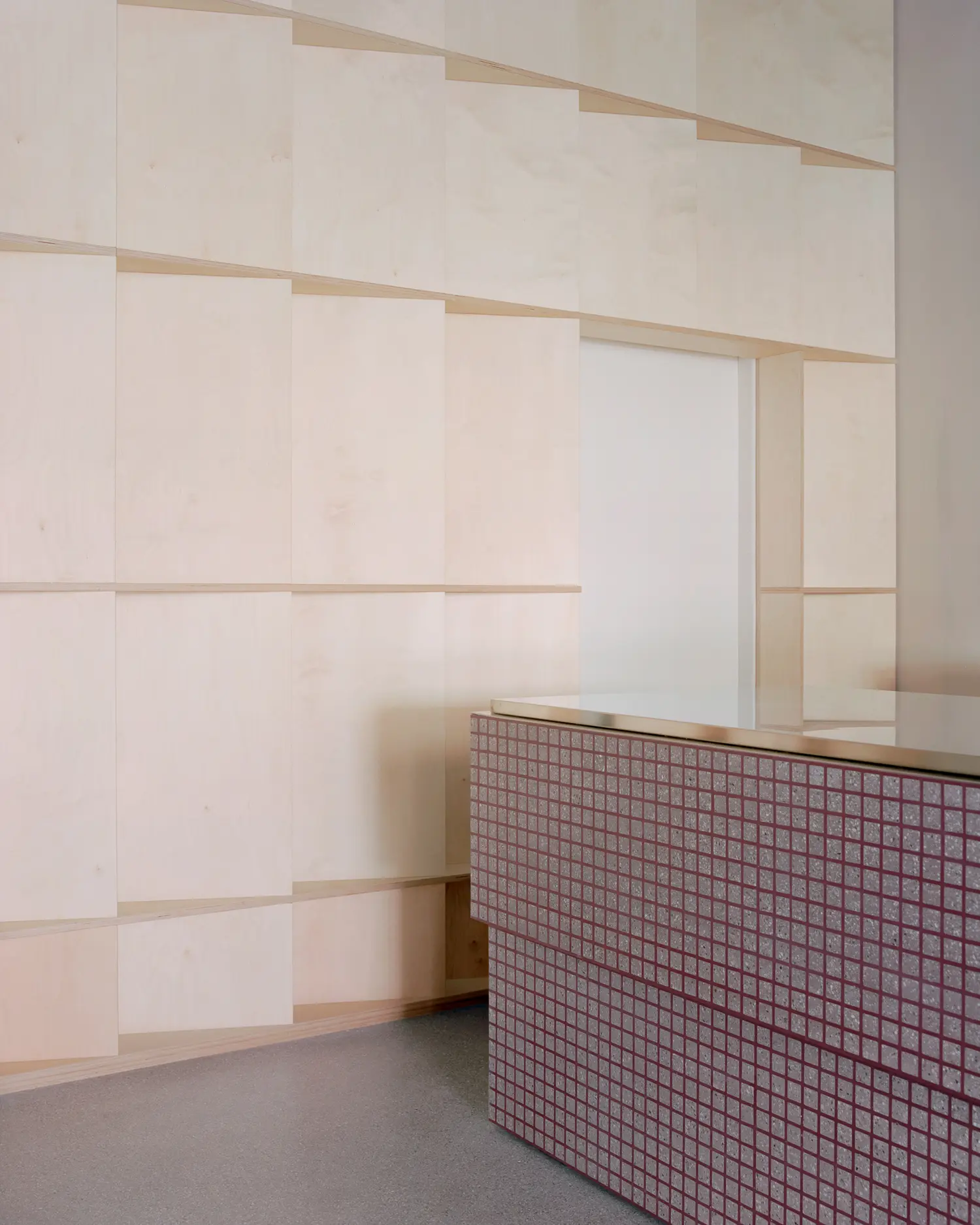 Close-up of a pinkish gridded counter with a polished metal top intersecting with a gridded birch wood paneled wall.