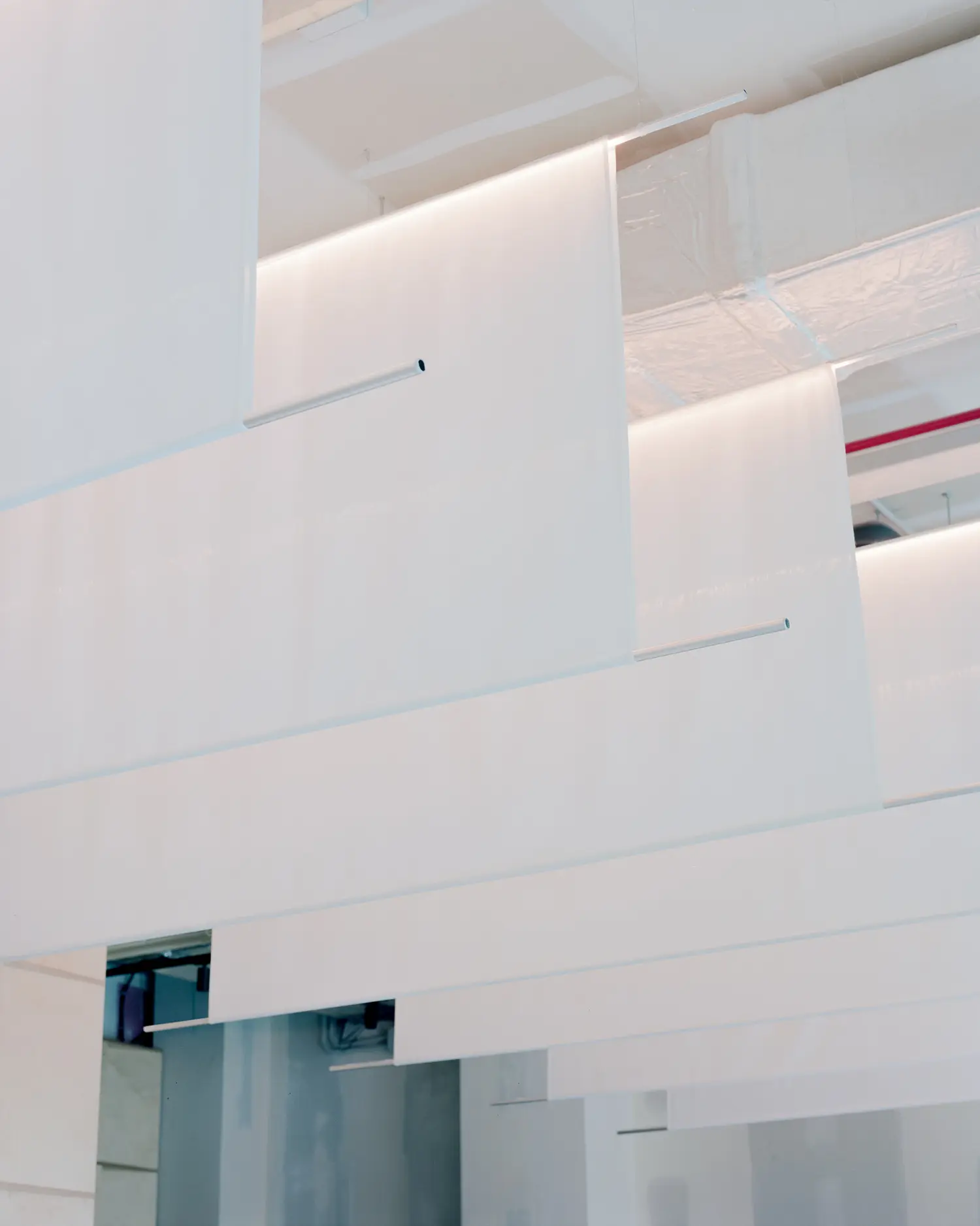 Low-angle view of white rectangular fabric panels suspended from an open ceiling with visible industrial ducts and pipes.
