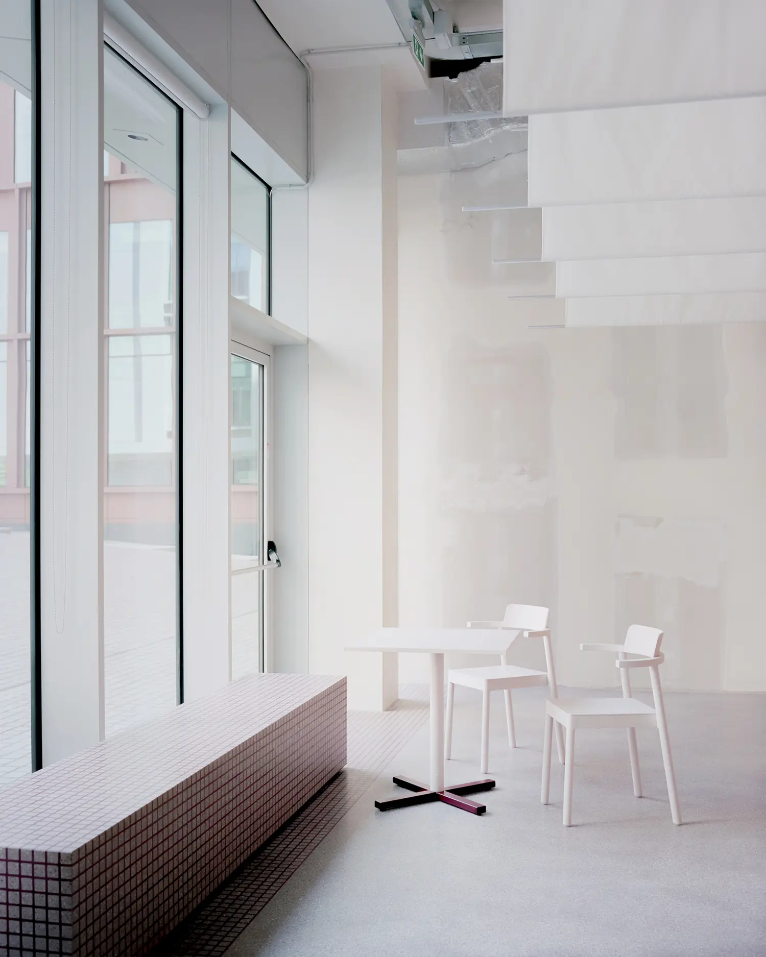Bright dining area with a long tiled window bench next to floor-to-ceiling glass windows overlooking an urban plaza.