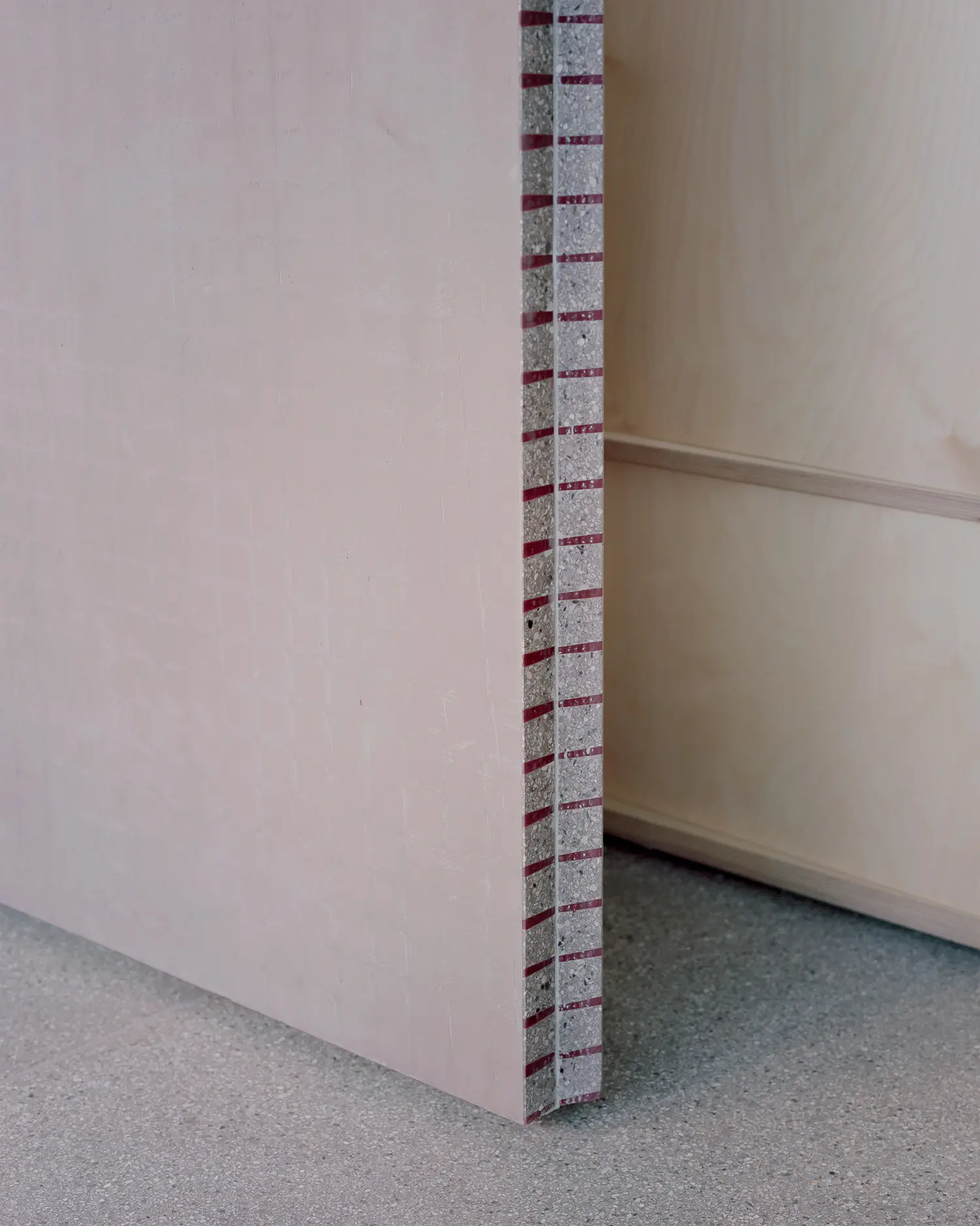 Macro detail of a structural panel edge showing a composite core layer with red grid markings next to a smooth birch wood surface.